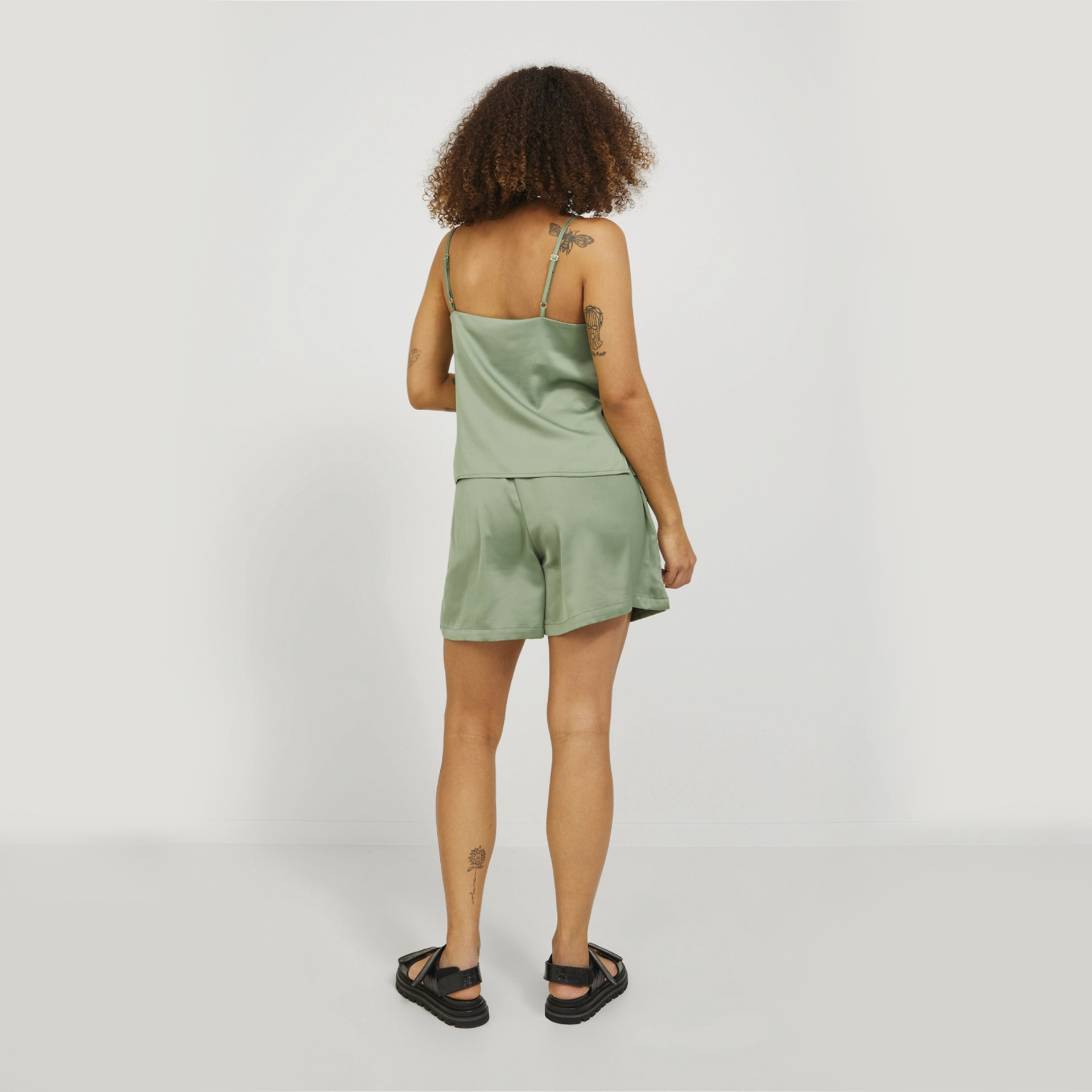 Conjunto de pijama verde claro acetinado com top de alças finas e calções, visto de costas