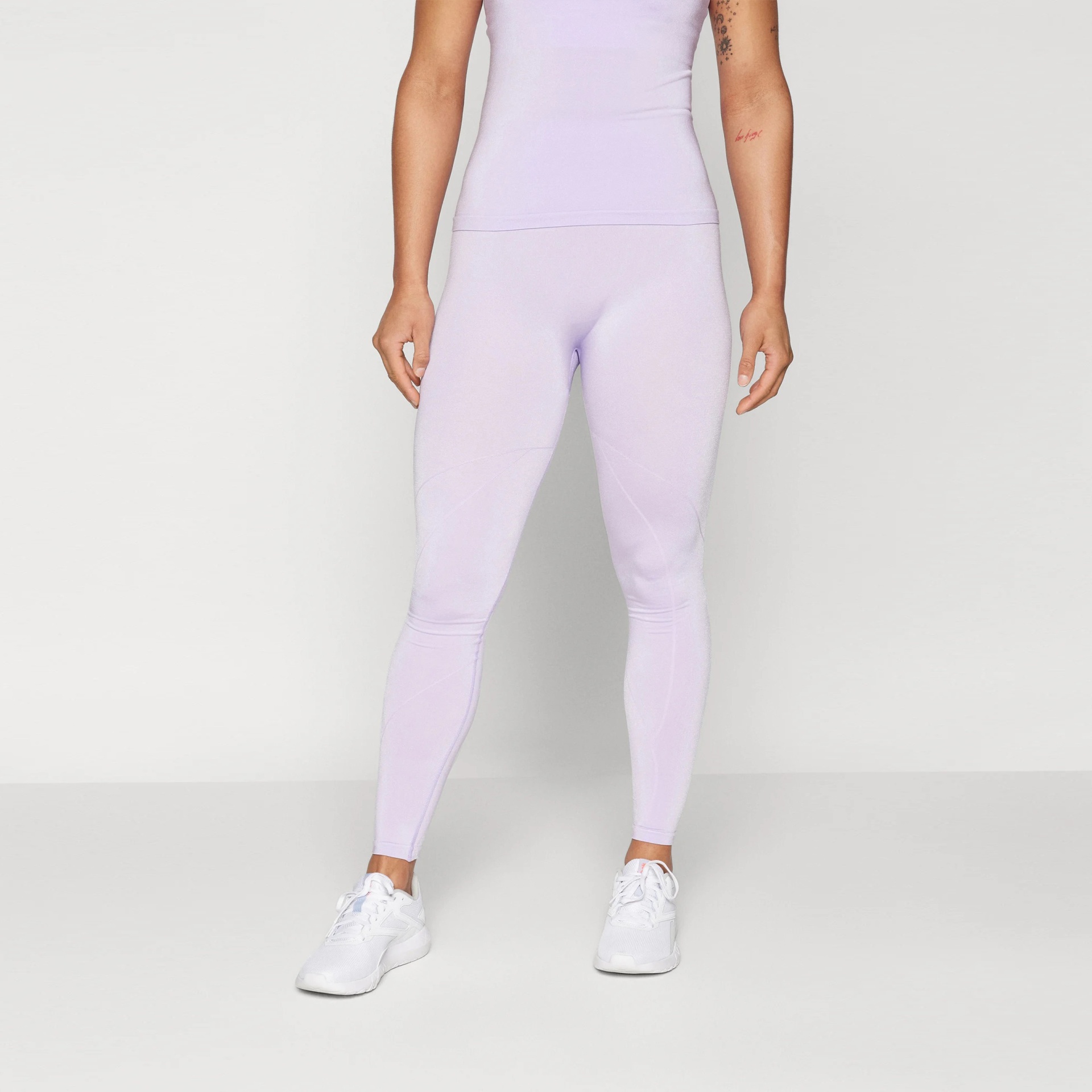 Leggings lilás de desporto usadas por mulher com sapatilhas brancas