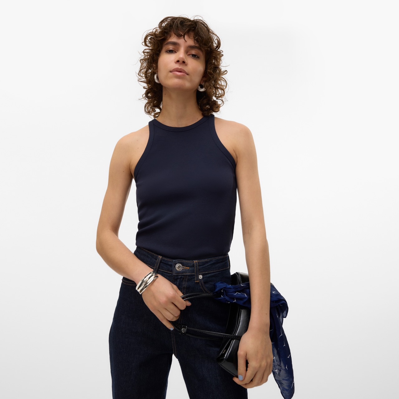 Mulher com top azul escuro, jeans e bolsa preta com lenço azul