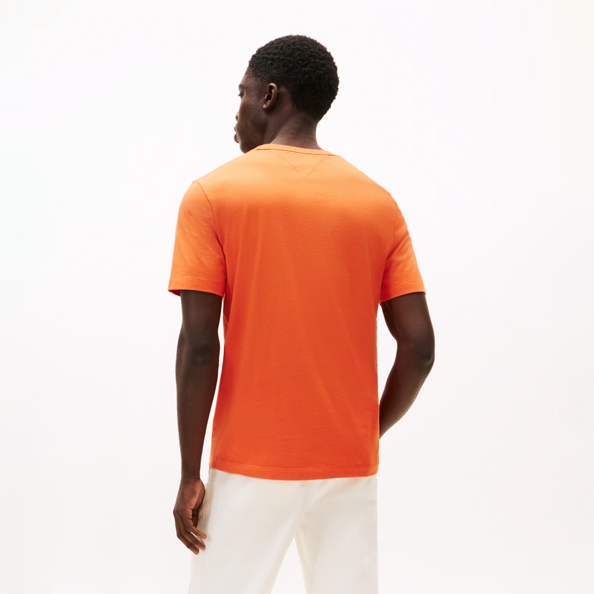 T-shirt laranja lisa de algodão vista de costas, com calças brancas num fundo branco.