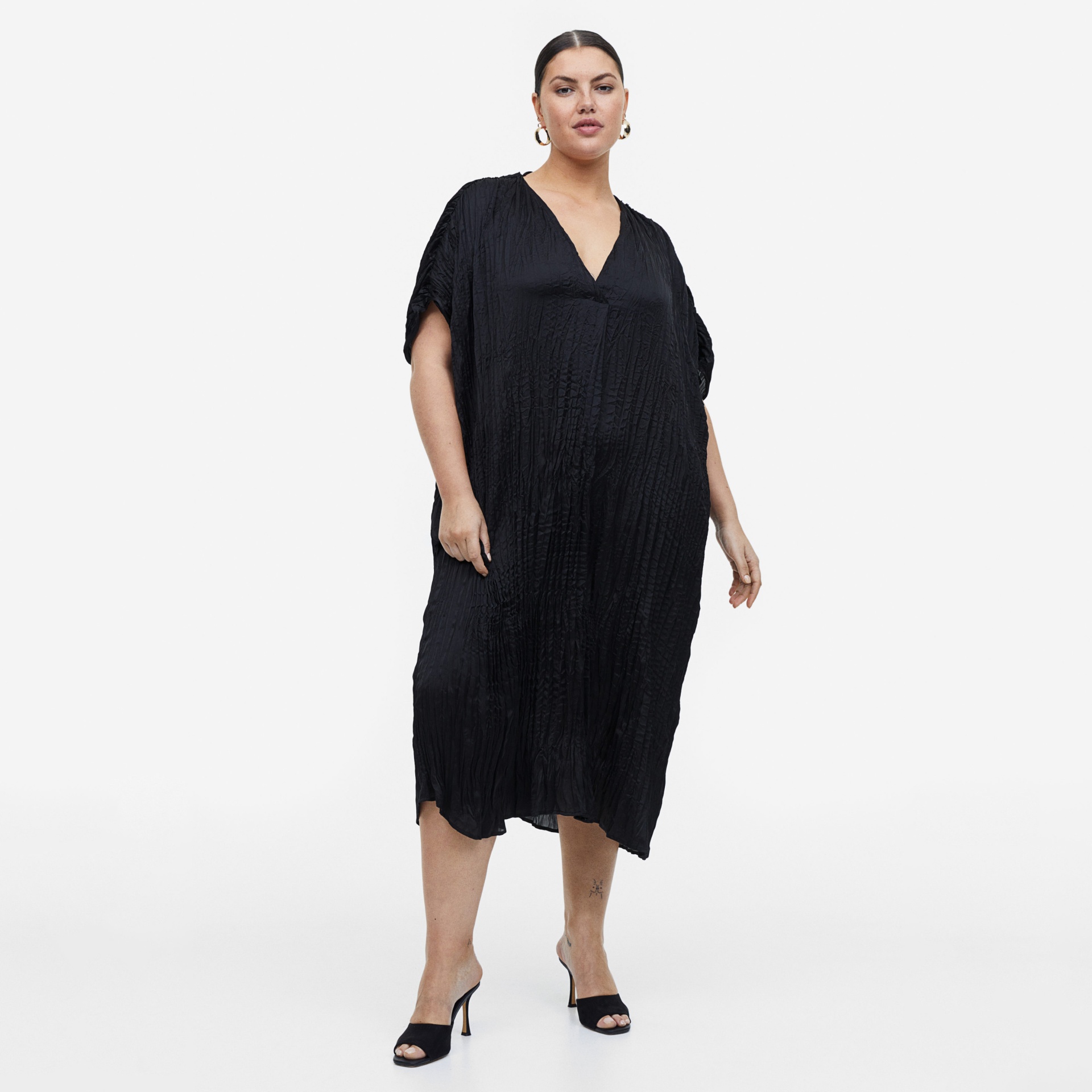 Vestido preto com decote em V e textura enrugada, usado por mulher