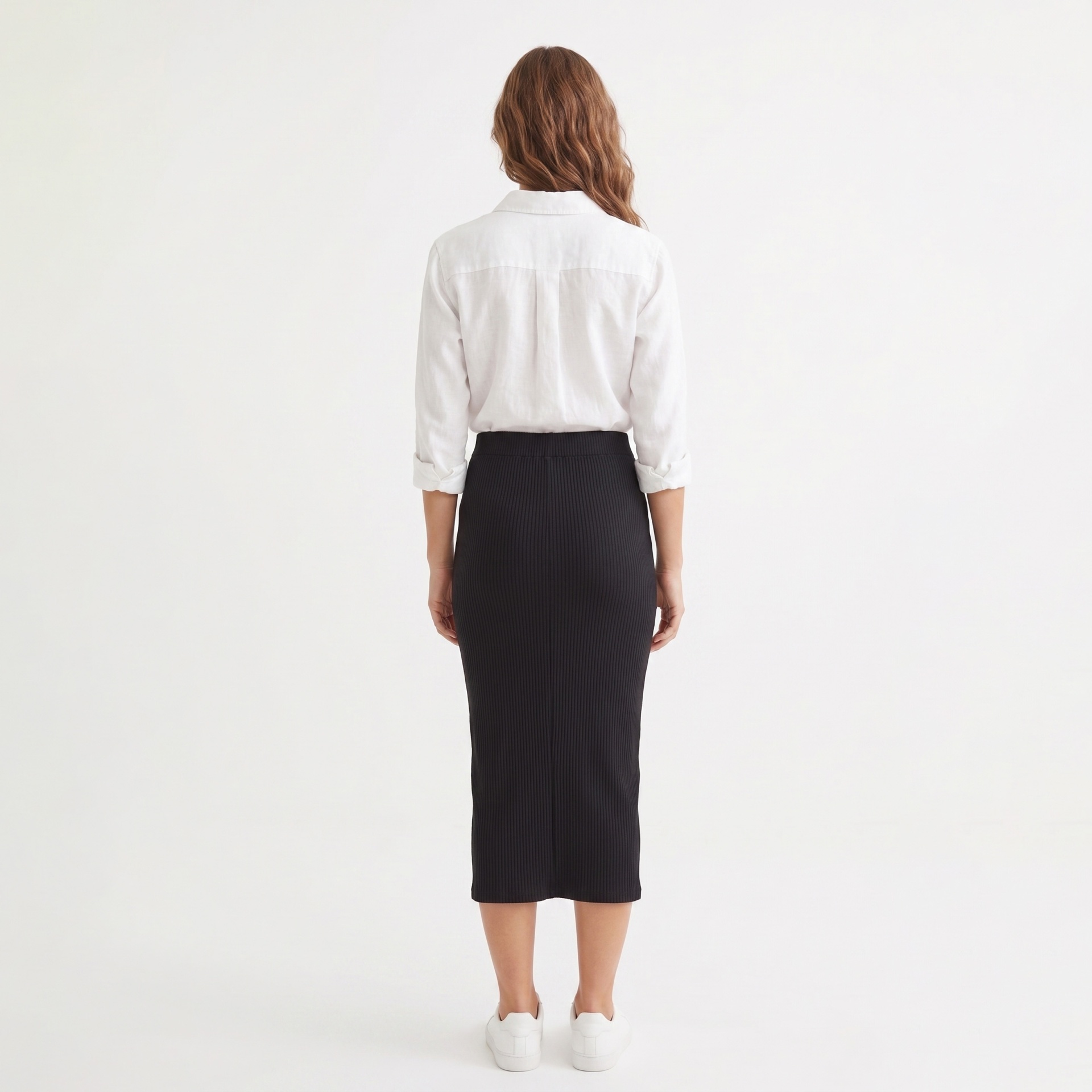 Mulher de costas com camisa branca e saia preta no fundo branco