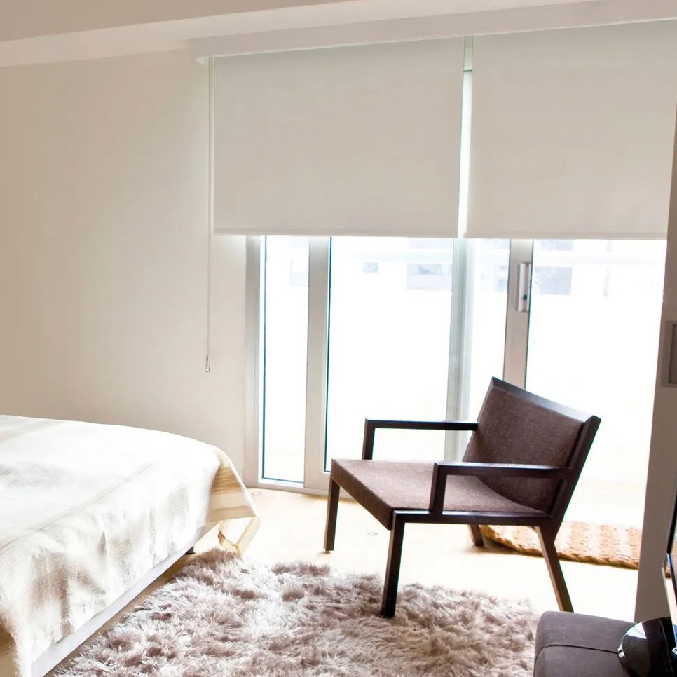 Quarto com cama branca, cadeira castanha, tapete peludo e persianas brancas