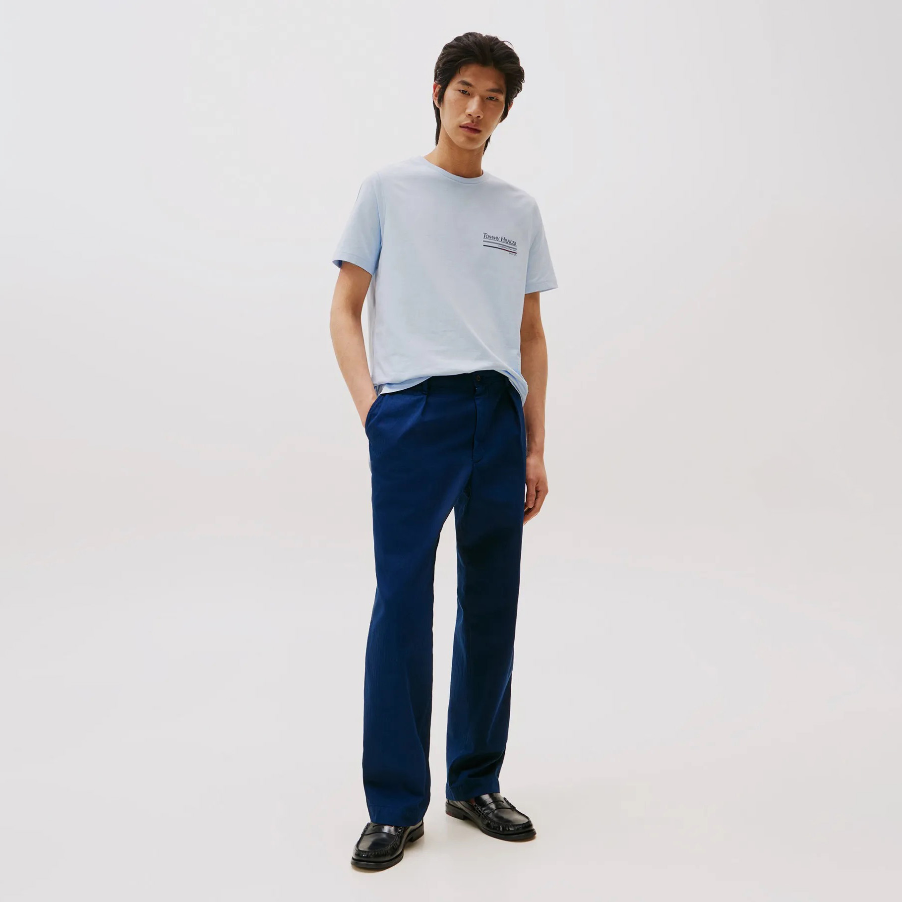 Homem a vestir camiseta azul clara, calças azuis escuras e sapatos pretos
