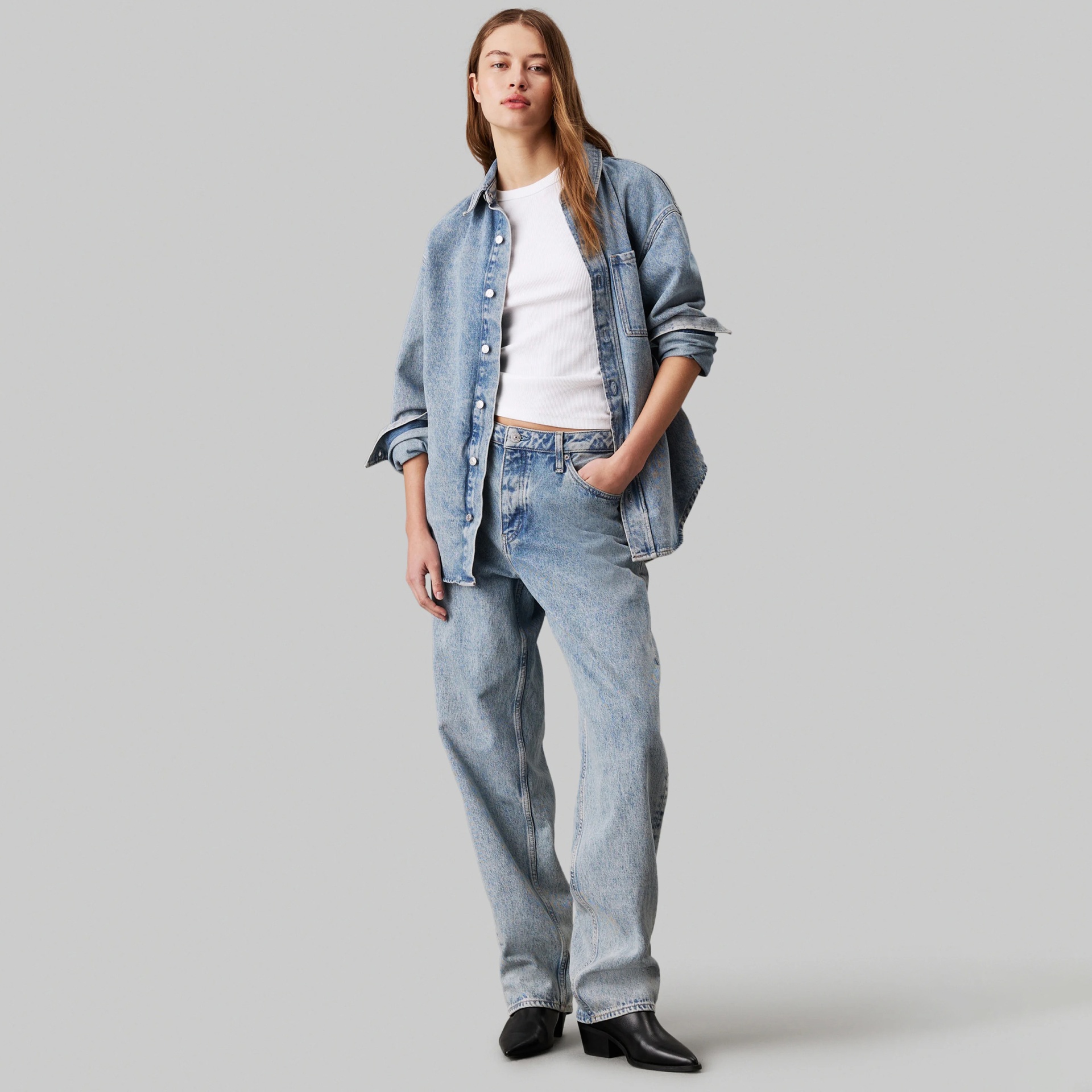 Modelo a usar camisa e calças de ganga azul clara com top branco e sapatos pretos