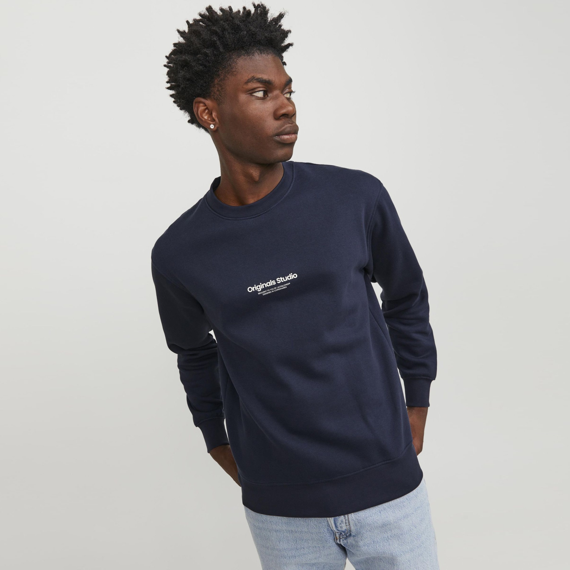 Sweatshirt azul escuro com logo branco no peito, usada por modelo de calças de ganga claras em fundo branco