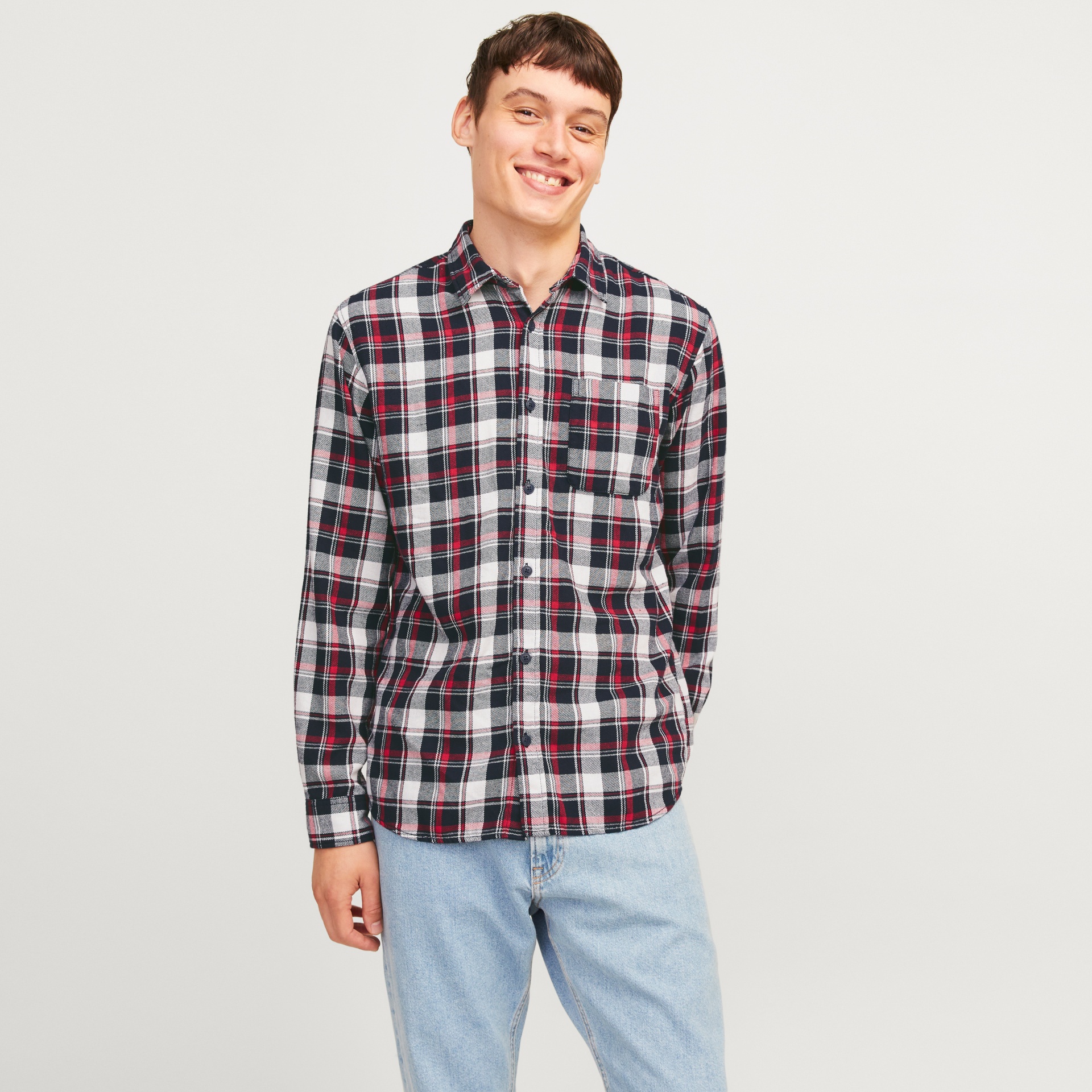 Homem sorridente a usar camisa de quadrícula preta, branca e vermelha com calças de ganga azul clara