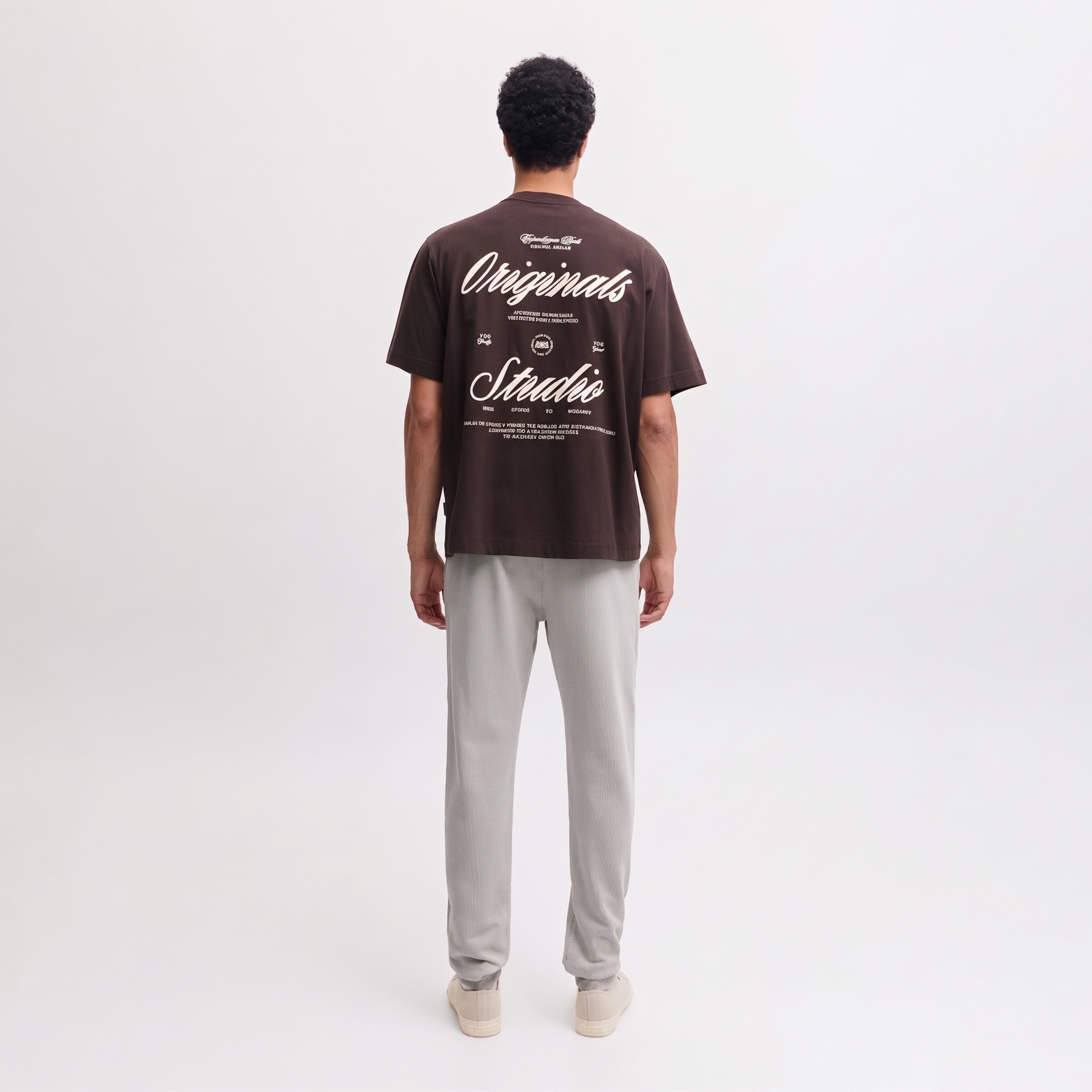 Homem de costas com t-shirt castanha com texto branco e calças claras