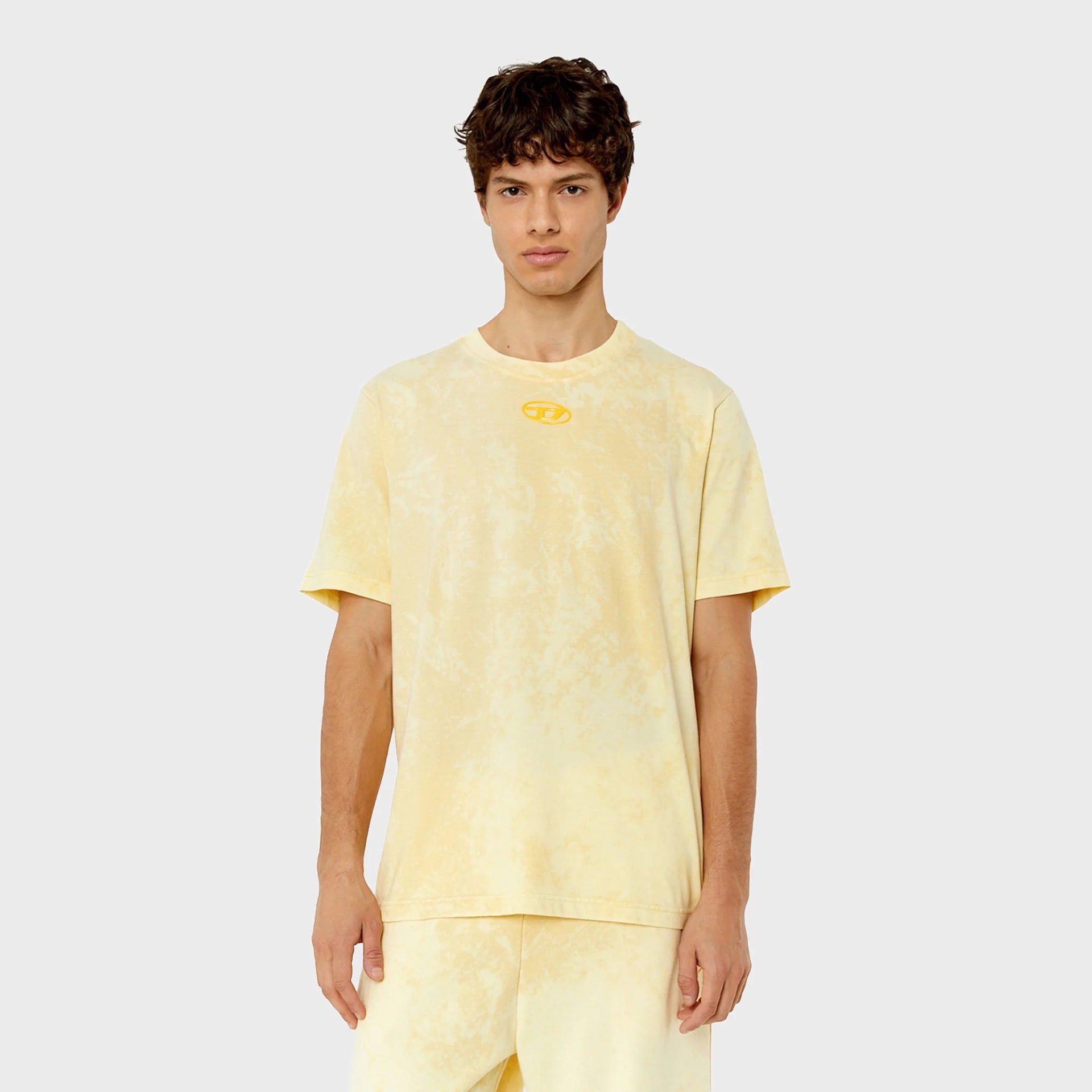 T-shirt amarela clara tie-dye com logótipo no peito, usada por modelo masculino