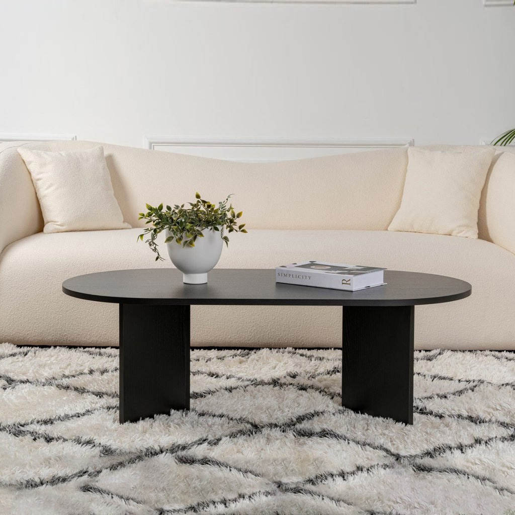 Mesa de centro preta oval em sala com sofá creme e tapete branco com padrão cinza.