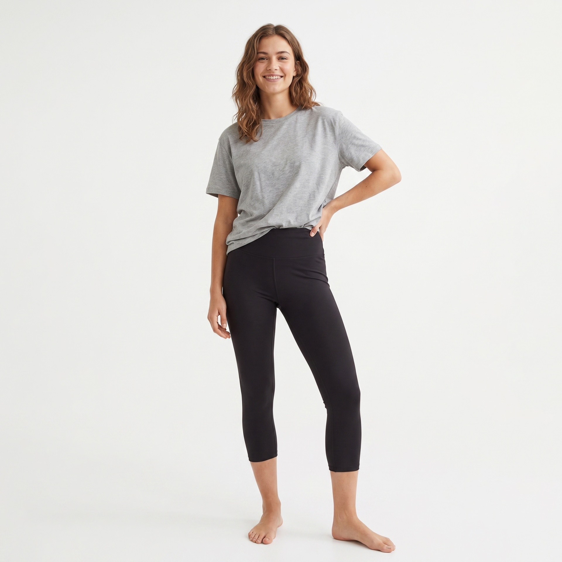 Mulher com t-shirt cinza e leggings pretas em fundo branco