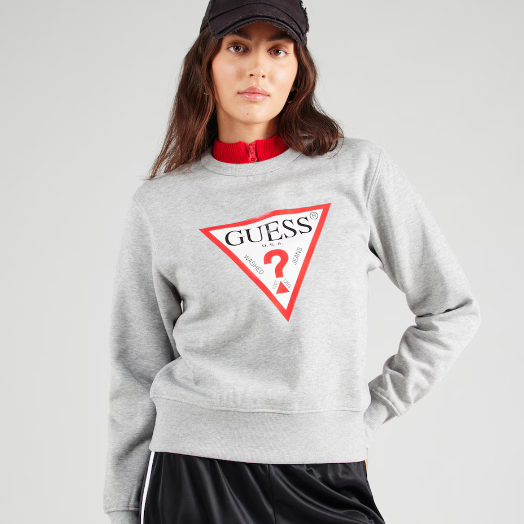 Mulher com sweatshirt cinza clara GUESS com logótipo triangular vermelho e boné preto