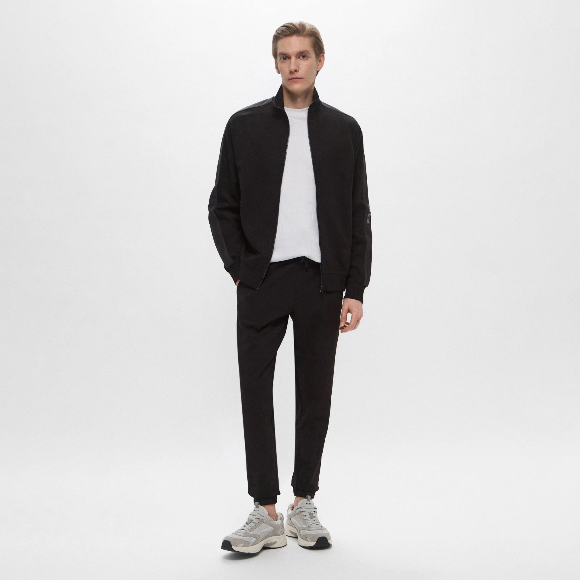 Homem a usar roupa casual preta e branca com sapatilhas desportivas, fundo branco