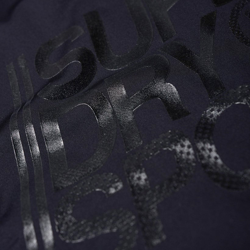 Detalhe de tecido preto com estampagem brilhante aberta com texto parcial SUPER DRY