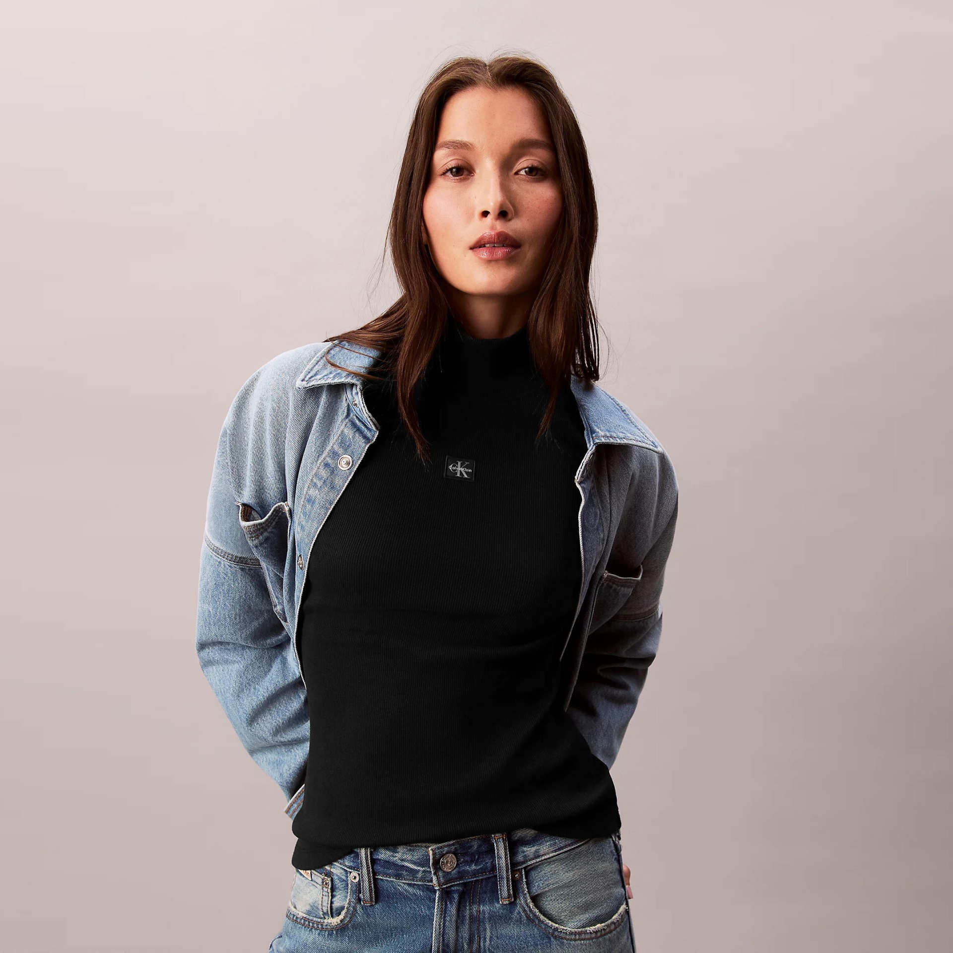 Mulher com camisola preta de gola alta, casaco e calças de ganga azul