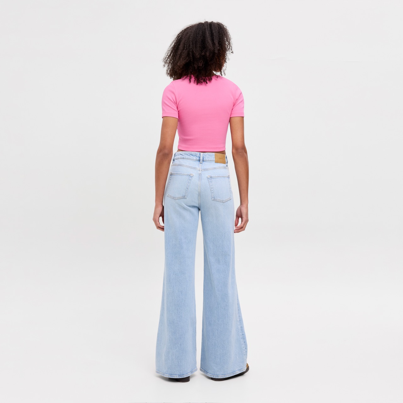 Pessoa vista de costas a usar calças de ganga largas azuis claras e t-shirt rosa de manga curta