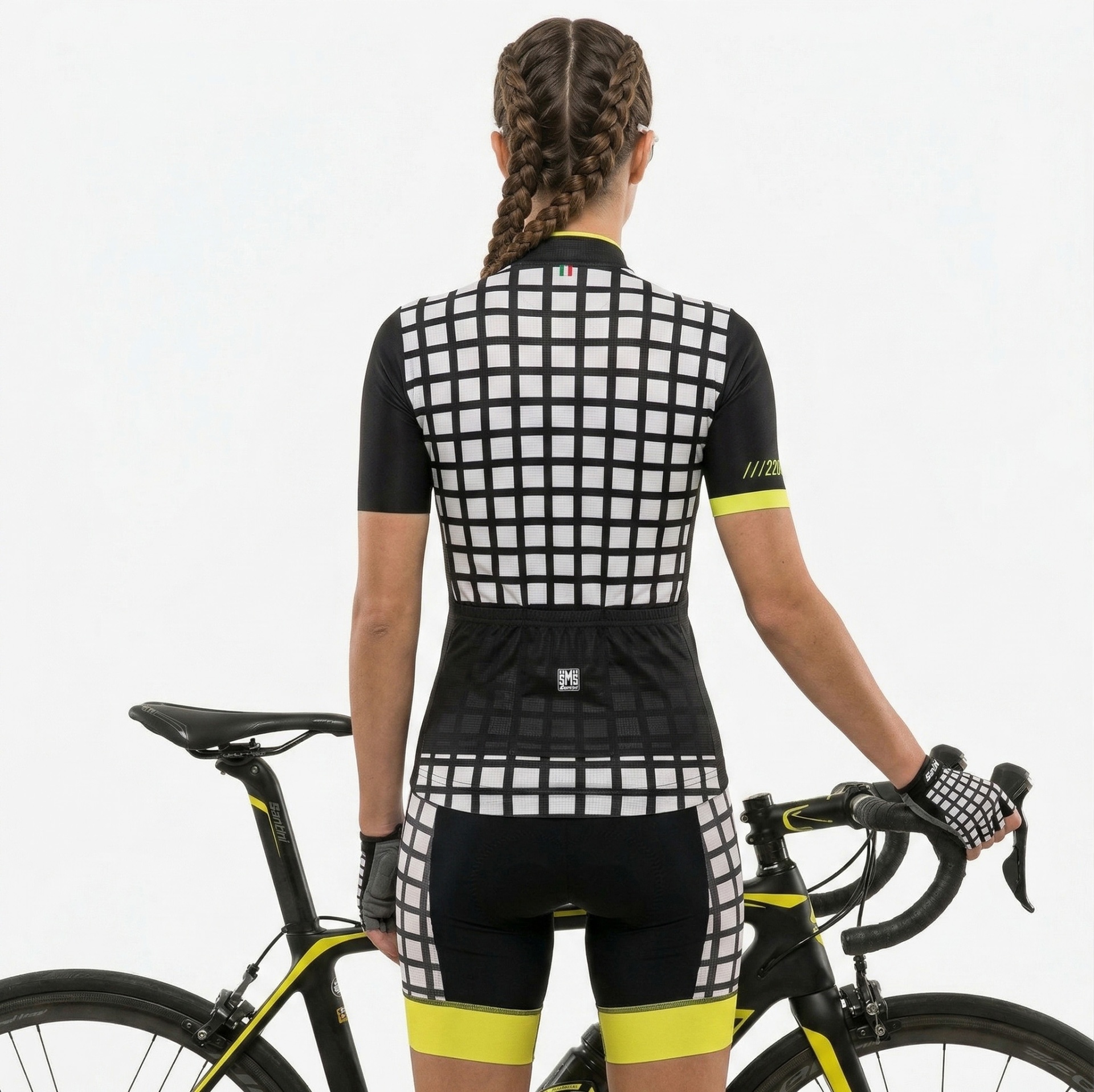 Conjunto de ciclismo feminino quadriculado preto e branco com detalhes amarelos junto a bicicleta preta e amarela