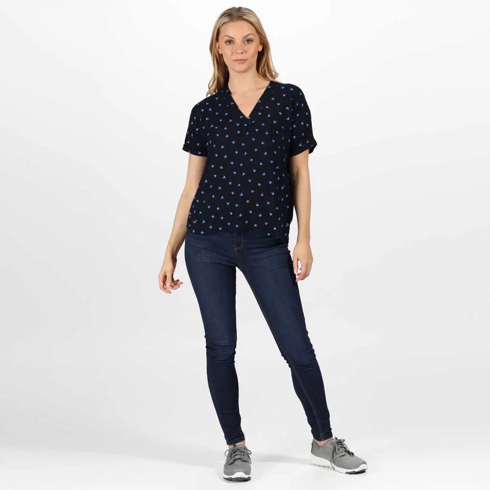 Mulher com blusa preta com padrão azul, jeans azul escuro e ténis cinzentos.