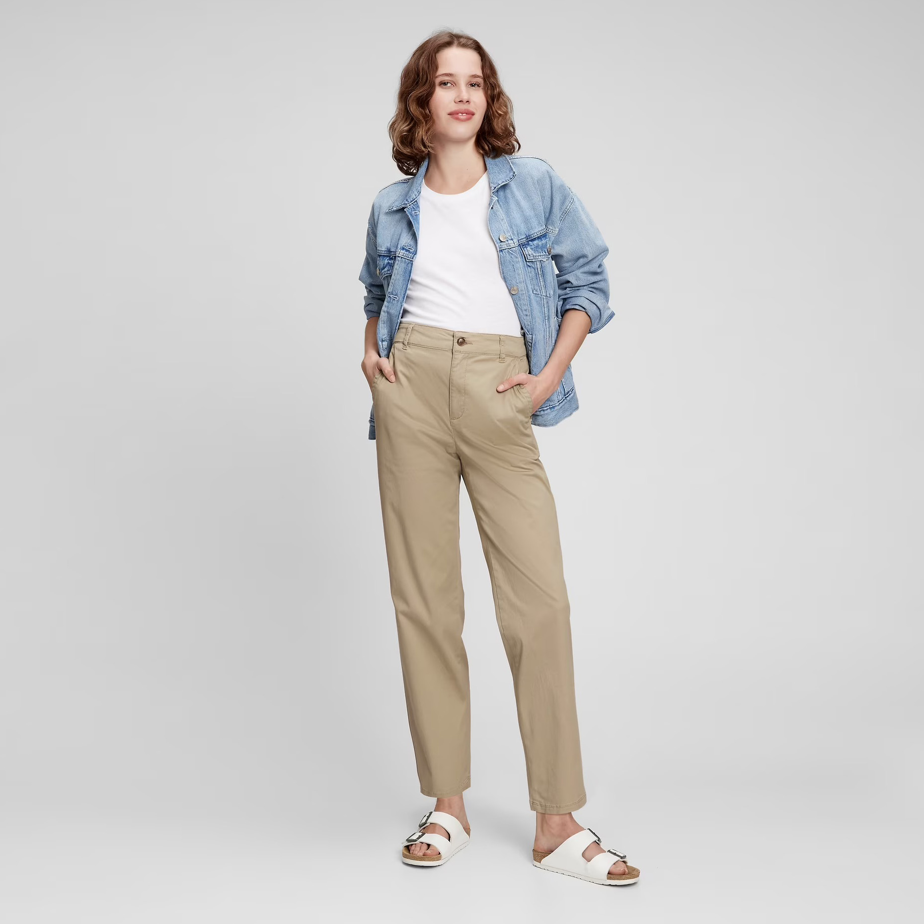 Mulher com calças bege, t-shirt branca, casaco de ganga azul e sandálias brancas