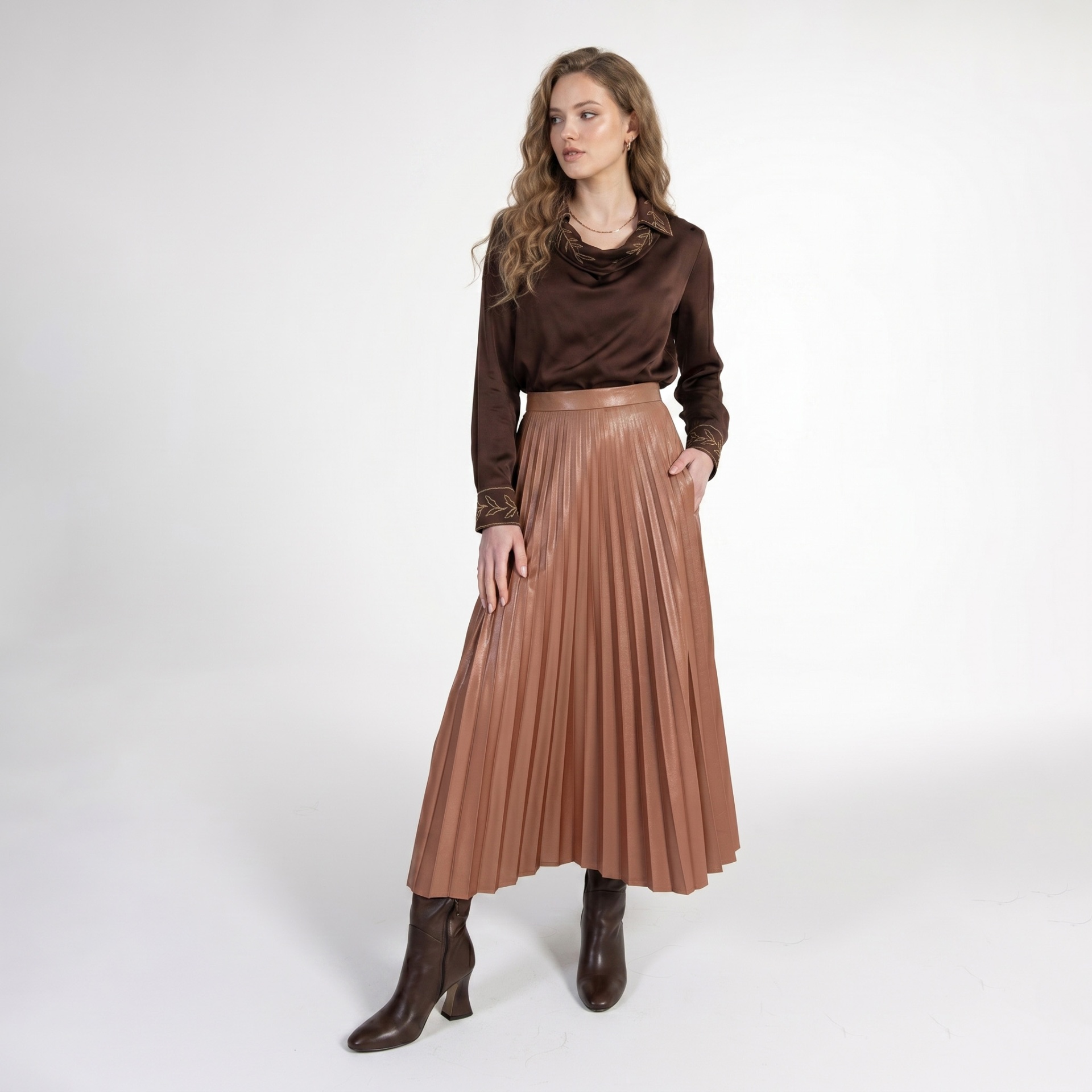 Mulher a vestir blusa castanha acetinada com detalhes bordados e saia plissada castanha clara com botas castanhas