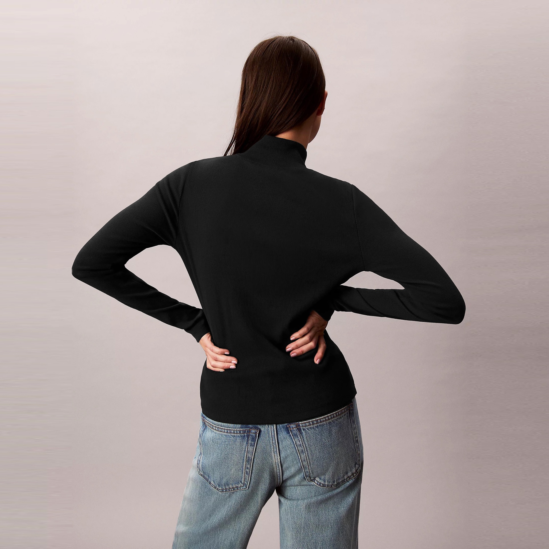 Pessoa de costas com camisola preta e calças de ganga azuis.