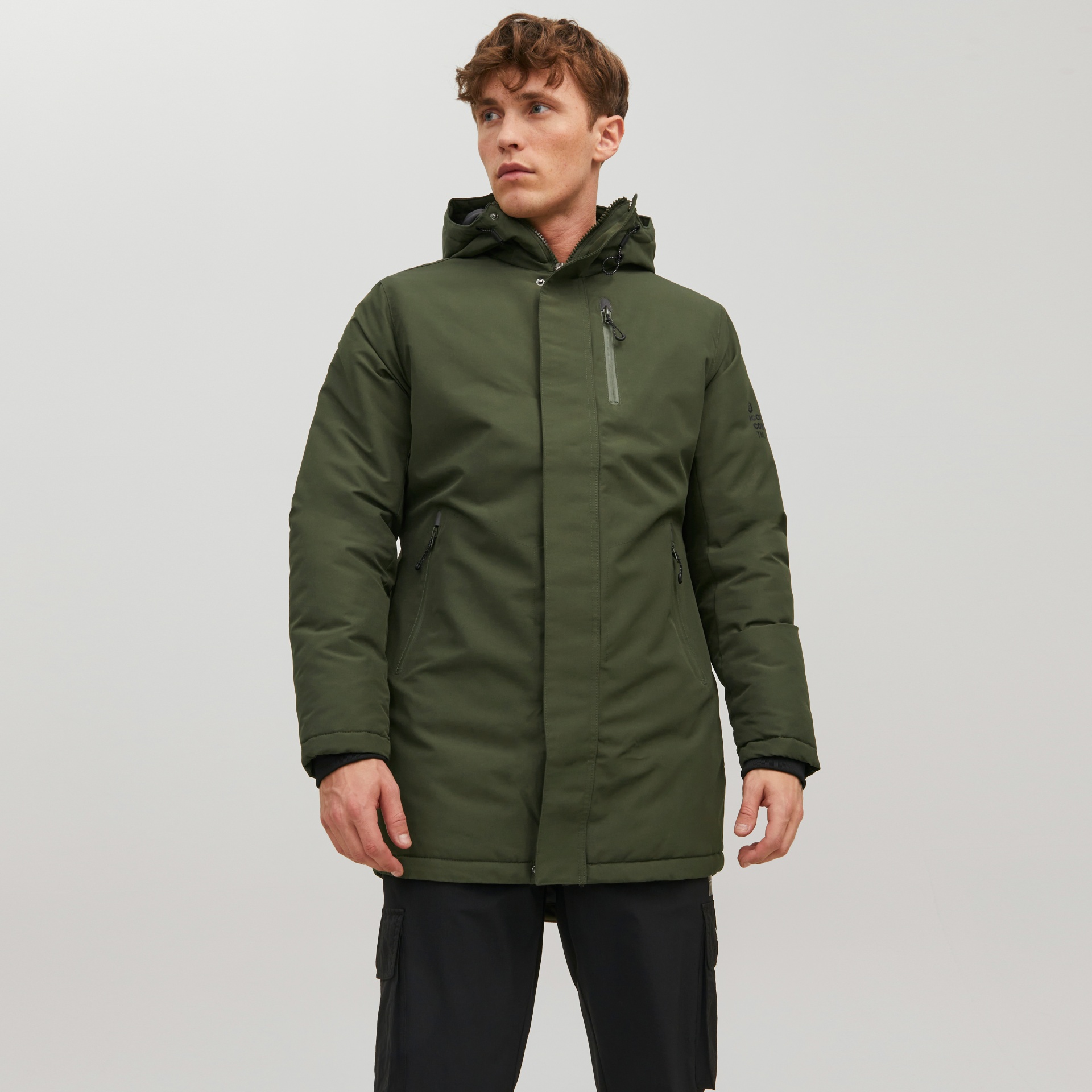 Homem com casaco verde-oliva acolchoado com capuz e calças pretas.