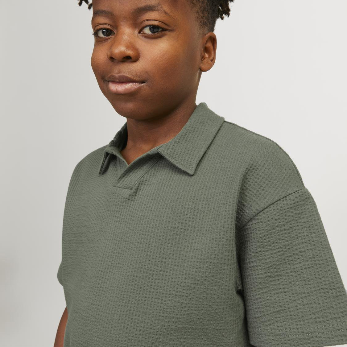 Menino com t-shirt verde-oliva de malha texturada, gola e manga curta, fundo branco
