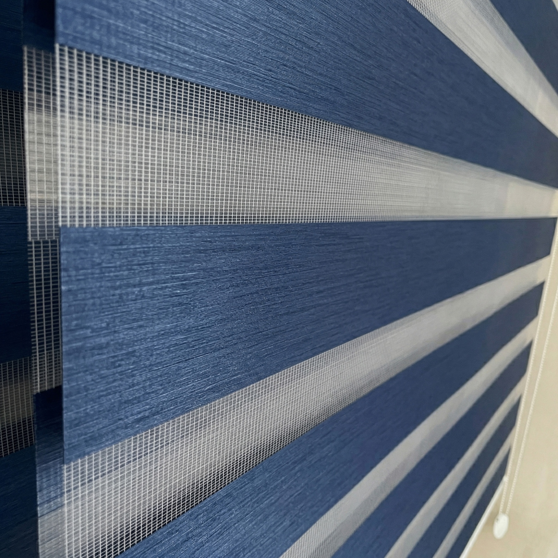 Estores de tecido azul e branco com faixas horizontais e corrente branca para ajuste