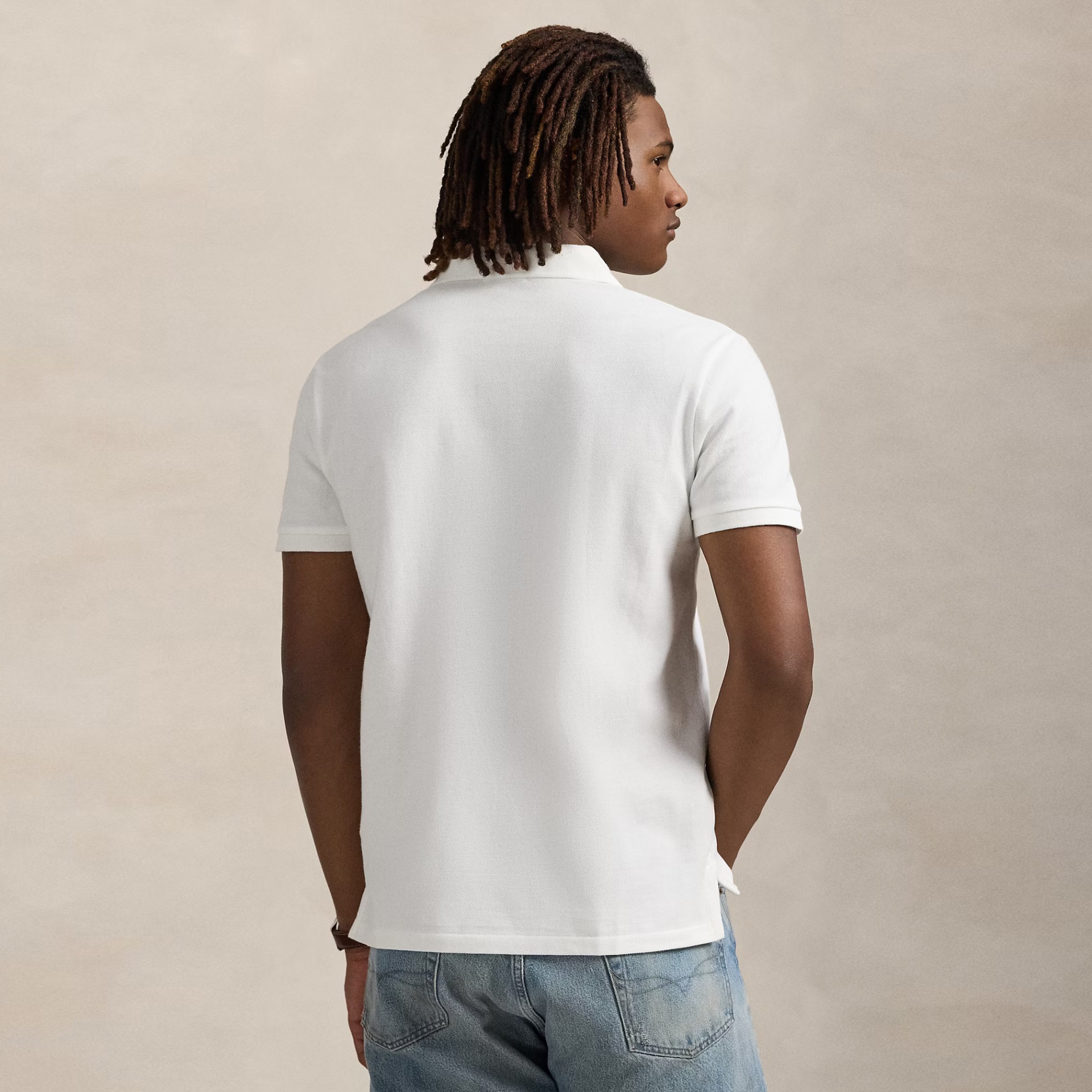 Homem de costas com t-shirt polo branca e jeans azuis claros