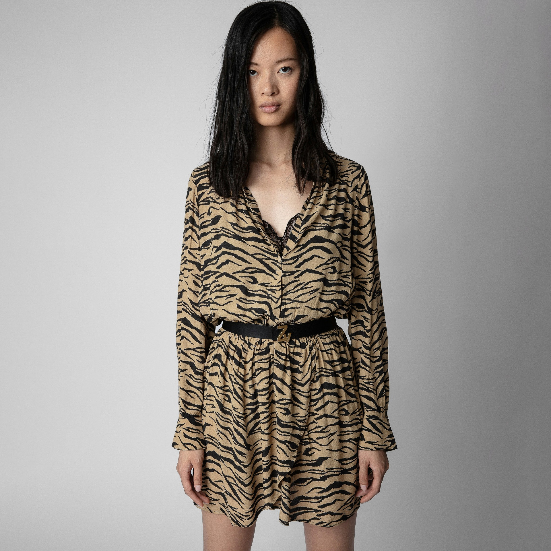 Vestido curto com padrão animal print bege e preto, cinto preto com fivela dourada, detalhe de renda preta no decote.