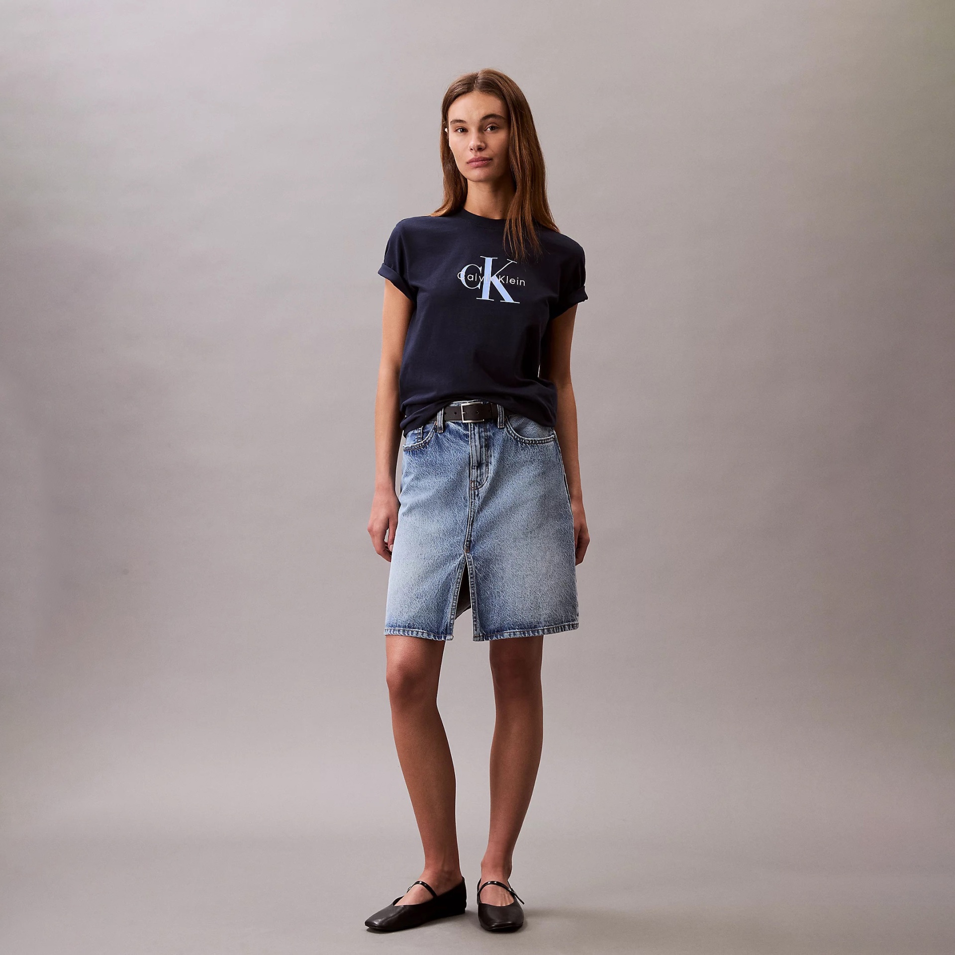 Mulher vestindo camisola preta com logo Calvin Klein, saia de ganga azul clara e sapatos pretos