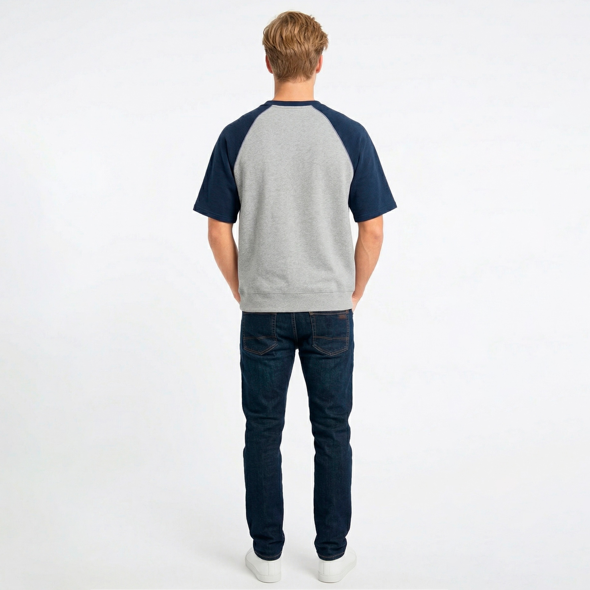 Homem a usar t-shirt cinzenta e azul escuro, jeans azul escuro e sapatilhas brancas vista de trás