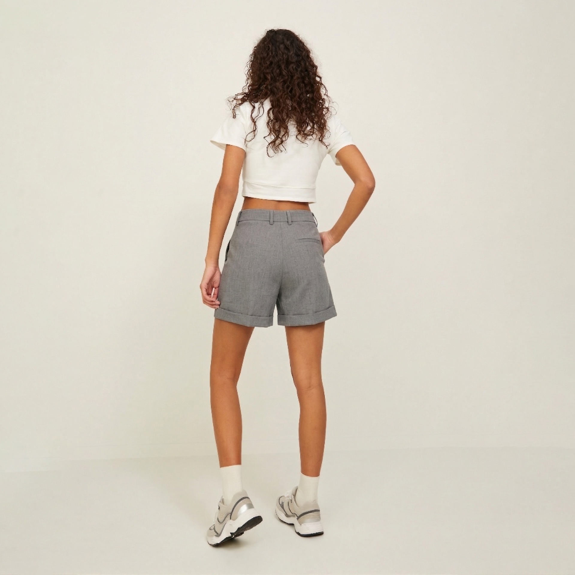 Mulher de costas com top branco, calções cinza e ténis brancos.