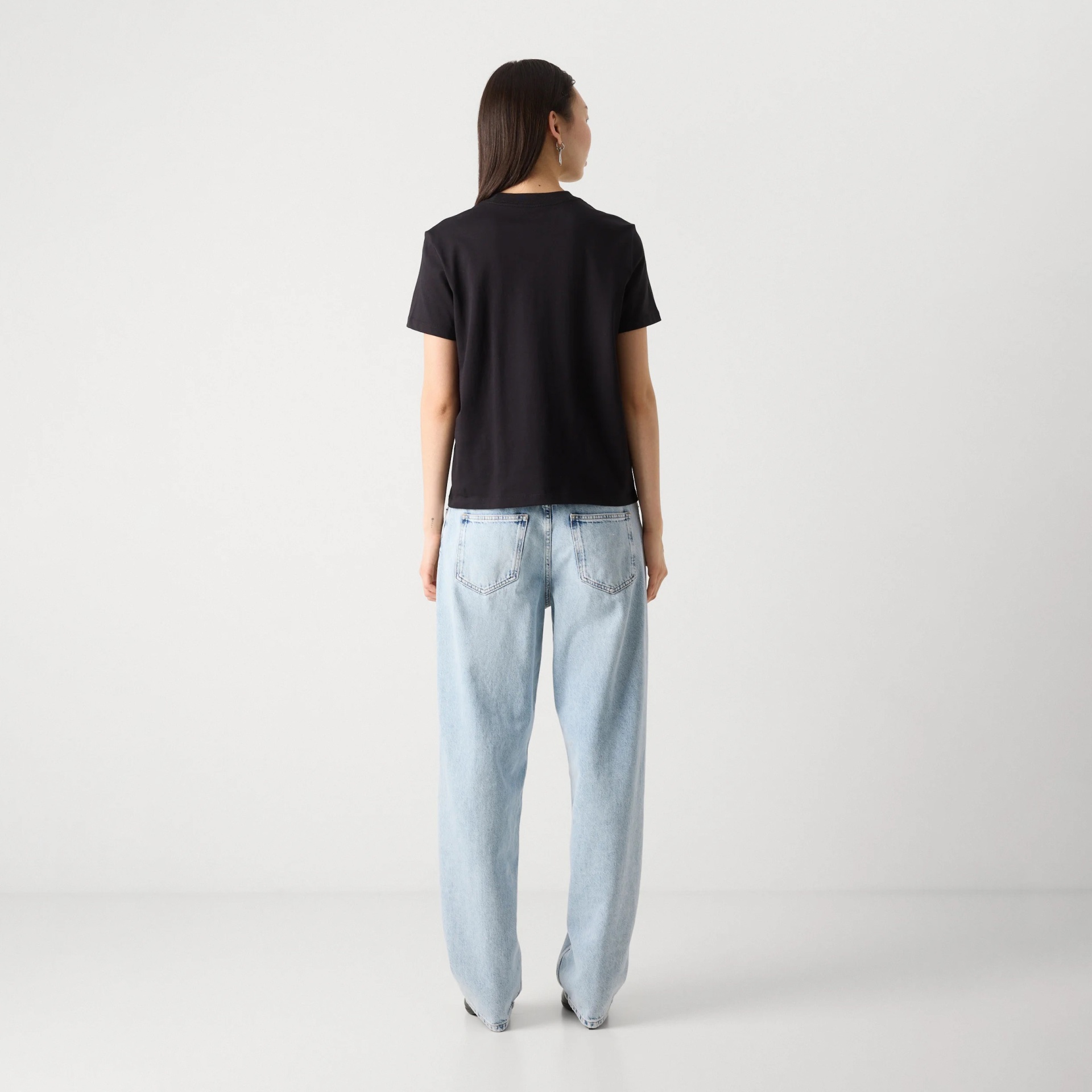 Pessoa de costas com t-shirt preta e calças de ganga azul claro