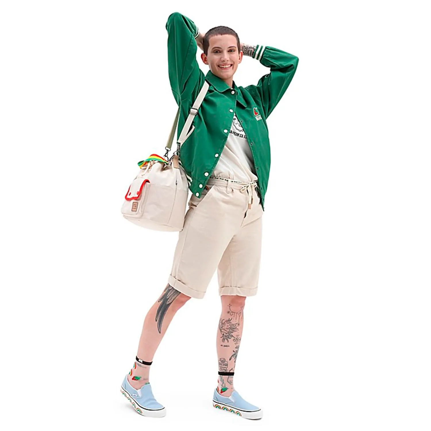 Pessoa com casaco verde, calções bege, sapatos azuis e mala bege com detalhes coloridos