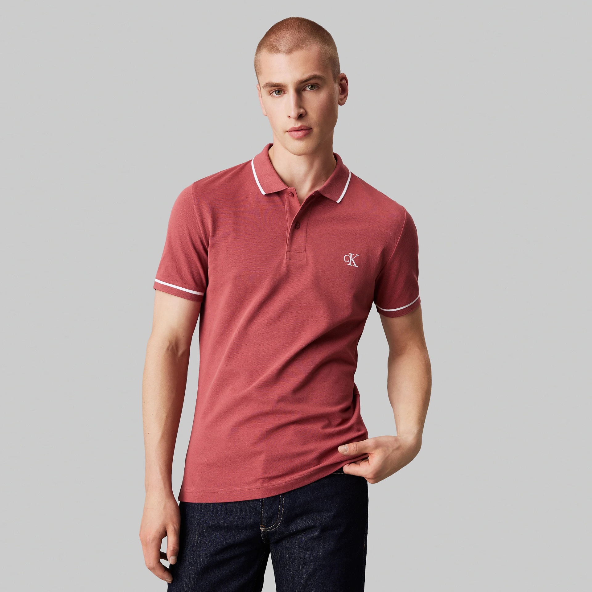 Polo rosa com detalhes brancos e logo cK bordado, usado por homem de pé