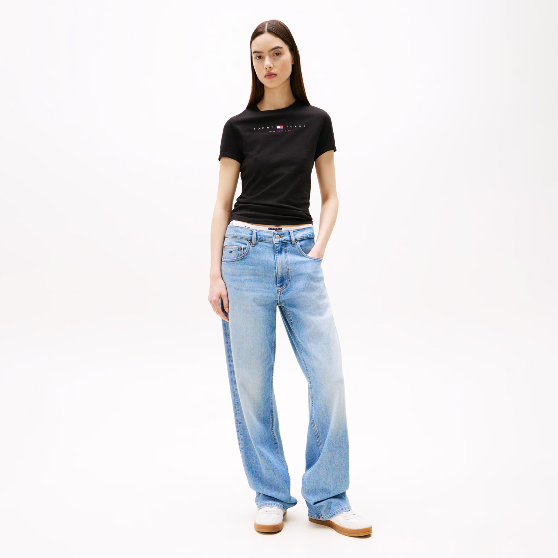 Mulher com camiseta preta Tommy Jeans e calças de ganga largas azuis