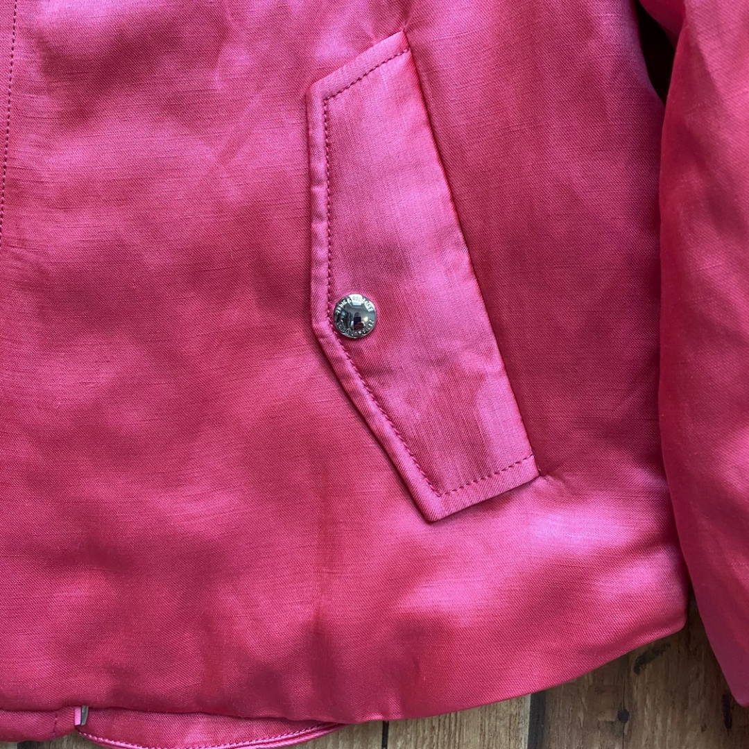 Casaco rosa com bolso e botão metálico em fundo de madeira