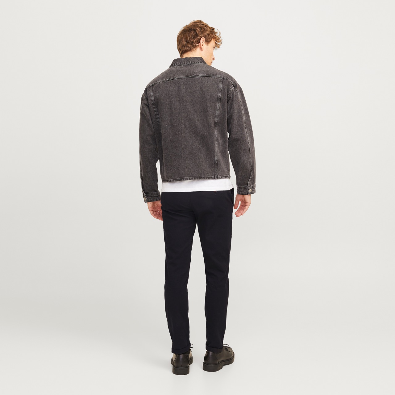 Homem de costas com jaqueta cinzento escuro, calças pretas e sapatos escuros