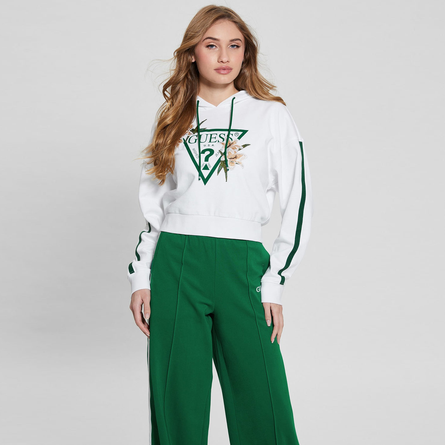 Mulher com sweatshirt branca de capuz e calças largas verdes com riscas
