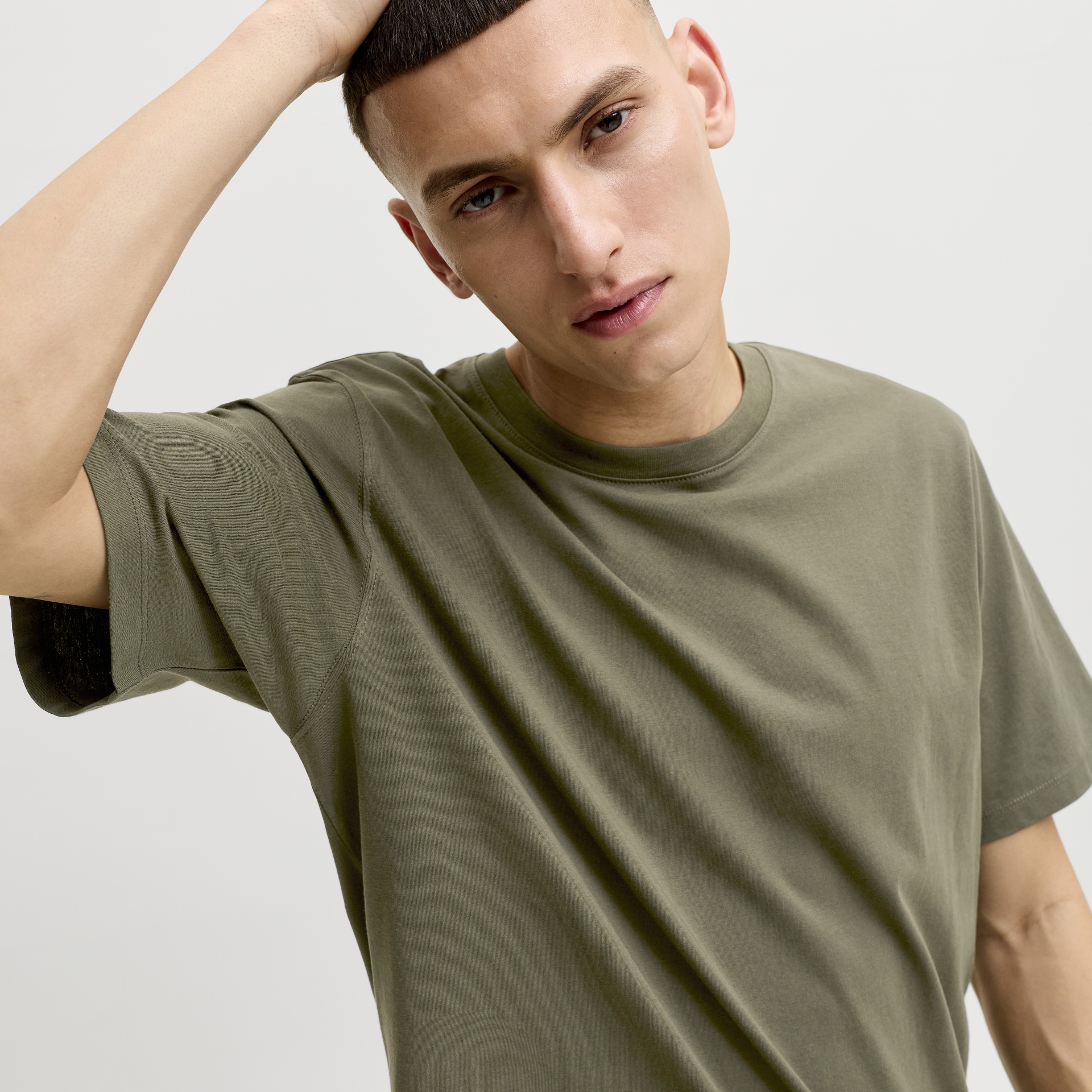 Homem com t-shirt verde-oliva de algodão e fundo cinza claro