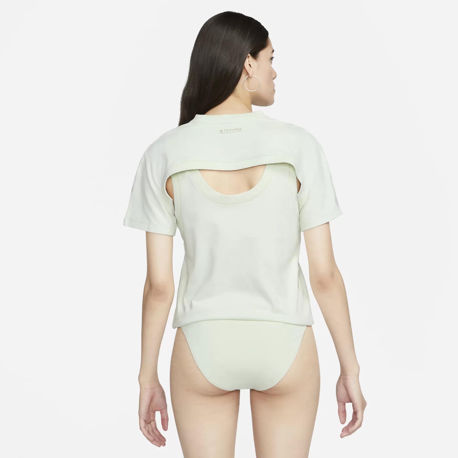 Mulher de costas com camisola verde clara e t-shirt curta por cima com abertura nas costas