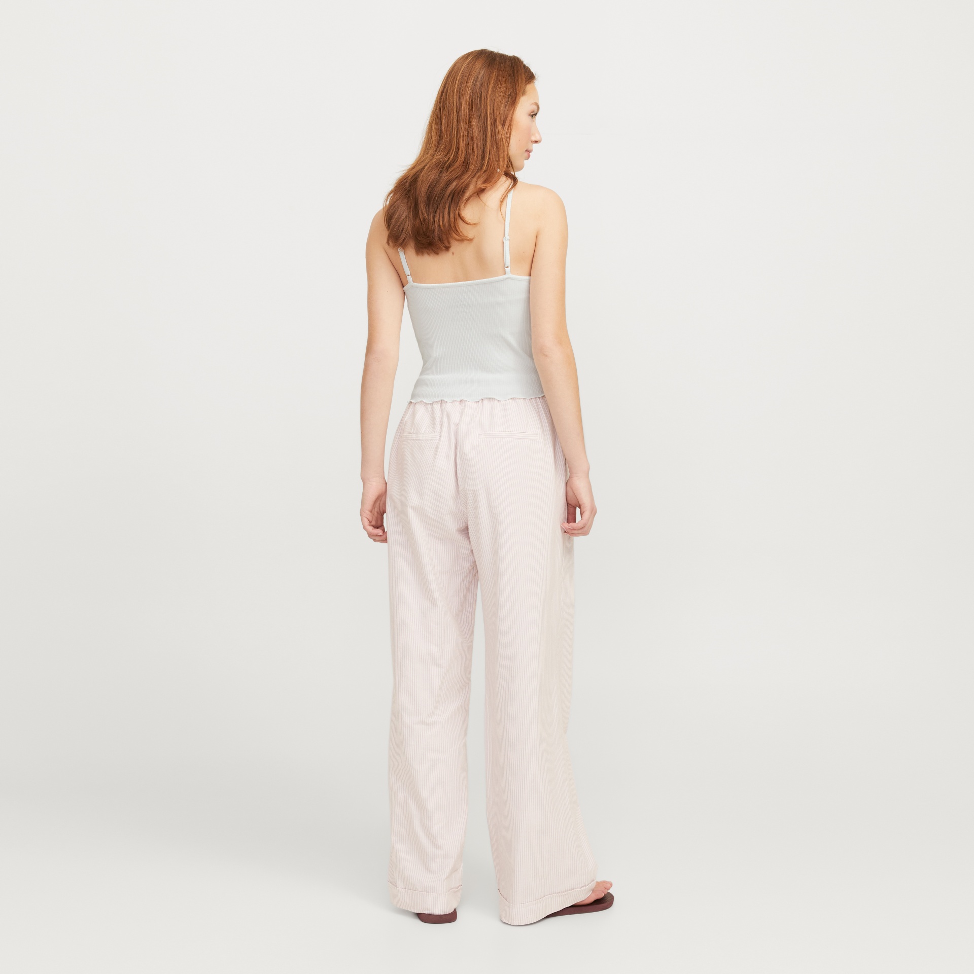 Mulher de costas com top branco e calças largas rosa claro riscas finas