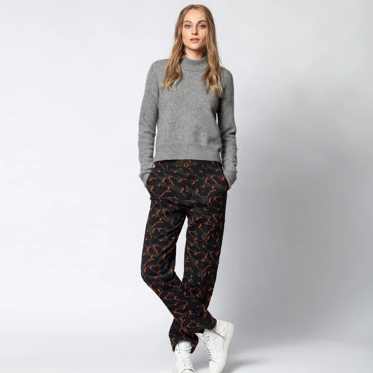 Mulher com camisola cinzenta de malha e calças pretas com padrão abstrato vermelho