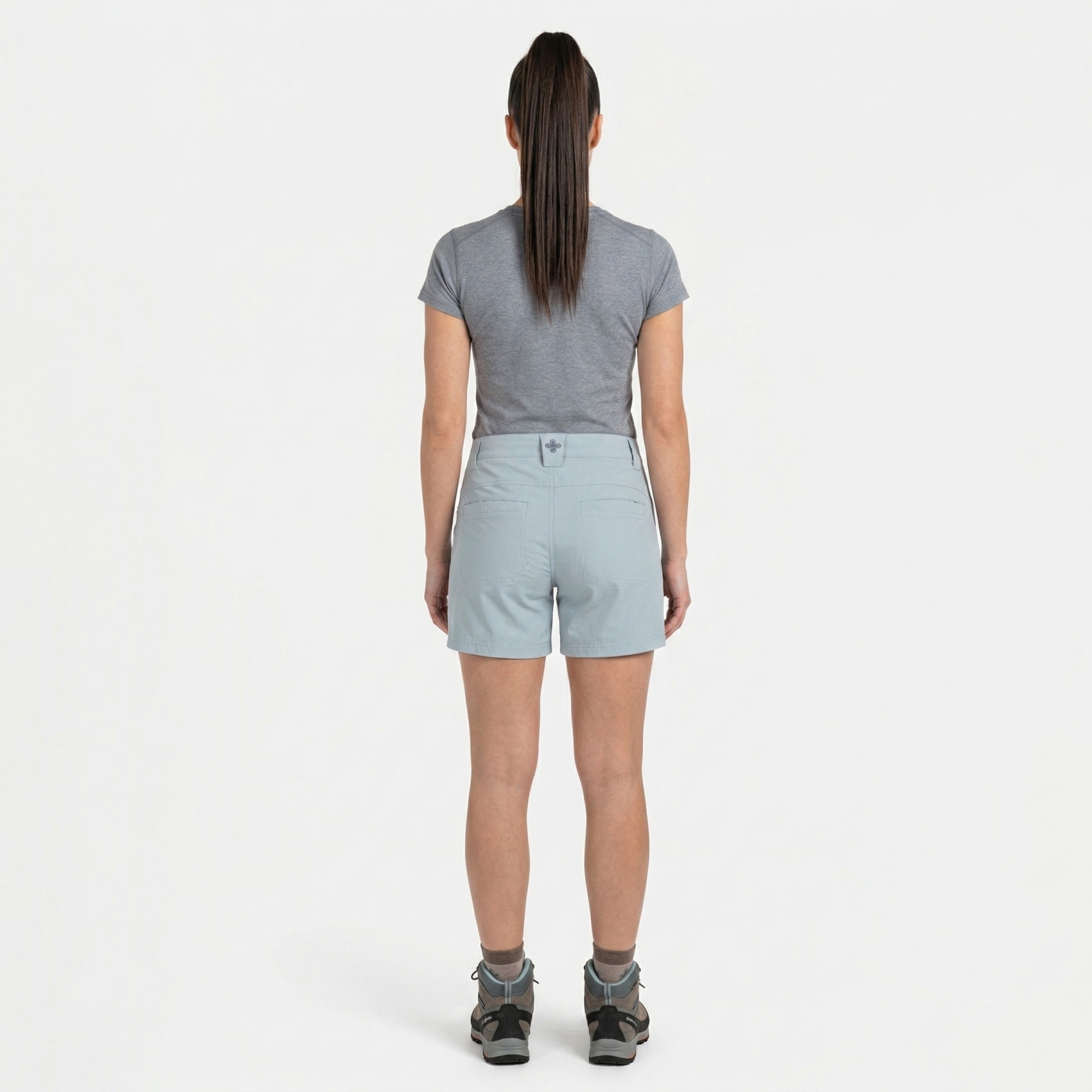 Mulher de costas com t-shirt cinzenta, calções cinza claros e sapatos de caminhada cinza e castanhos