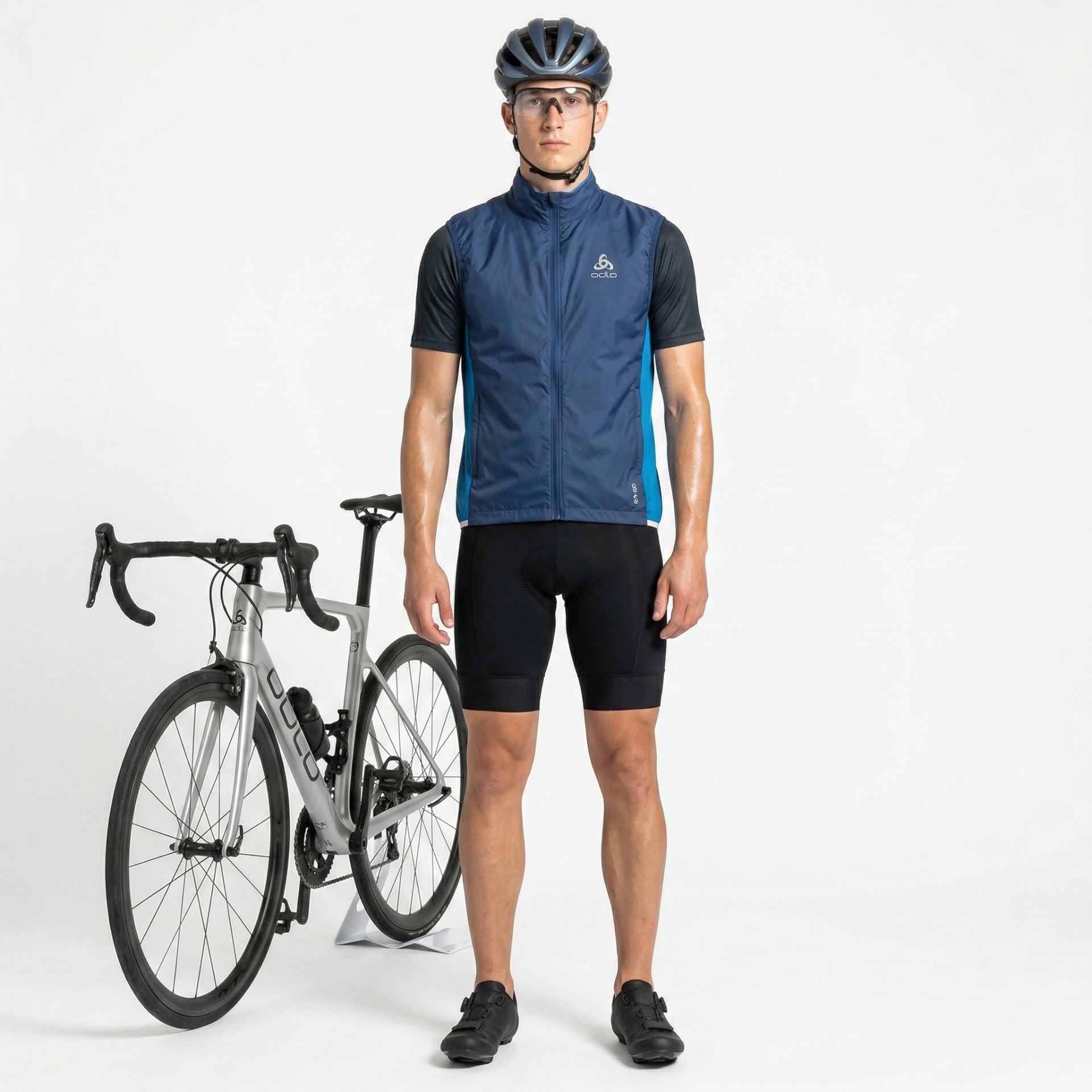 Homem com roupa de ciclismo azul e preta ao lado de bicicleta cinzenta.