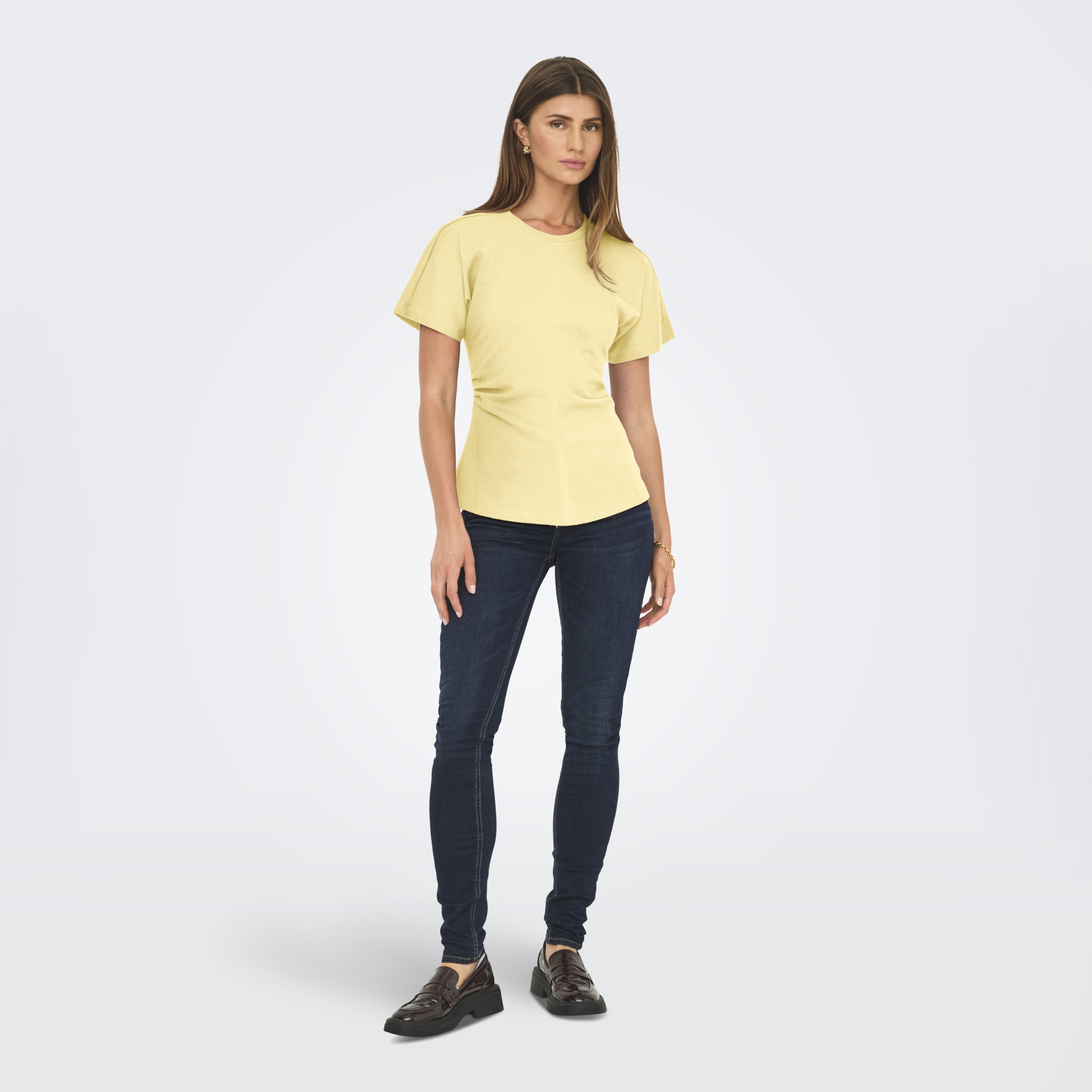 Mulher com camisola amarela, jeans escuros e sapatos castanhos.