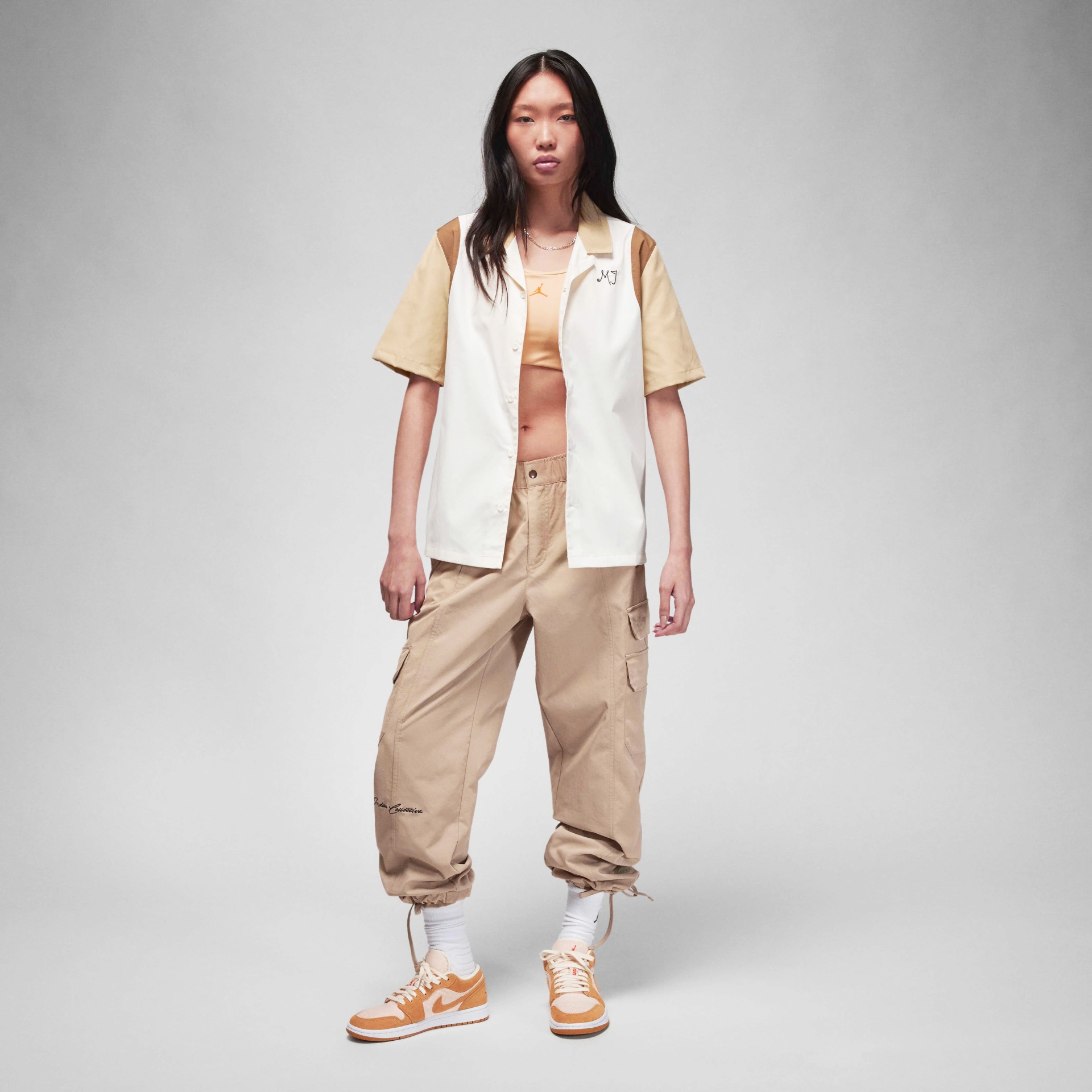 Mulher a usar roupa desportiva casual em tons bege, branco e laranja, num fundo cinza claro.