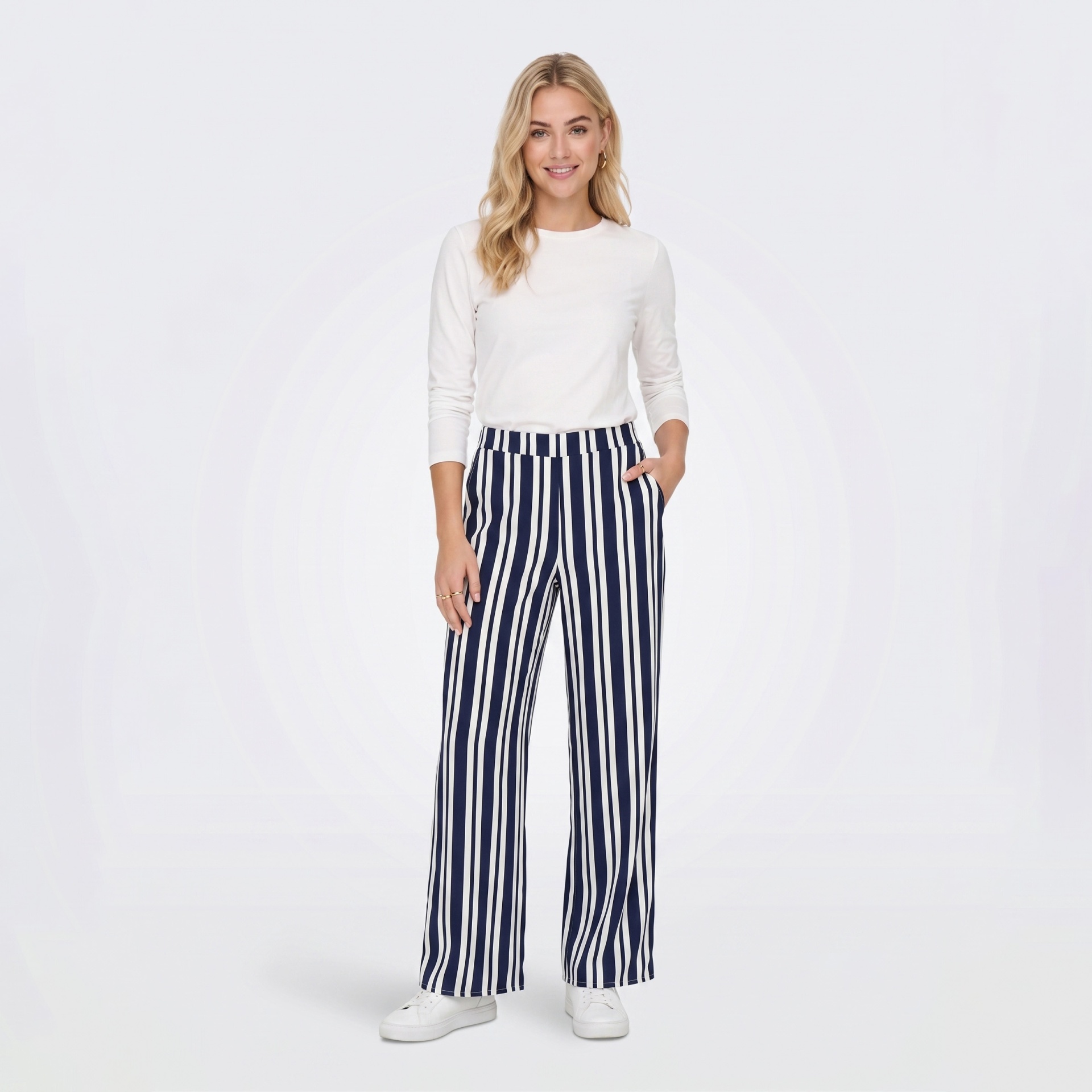 Mulher com camisola branca e calças às riscas azuis e brancas em fundo branco