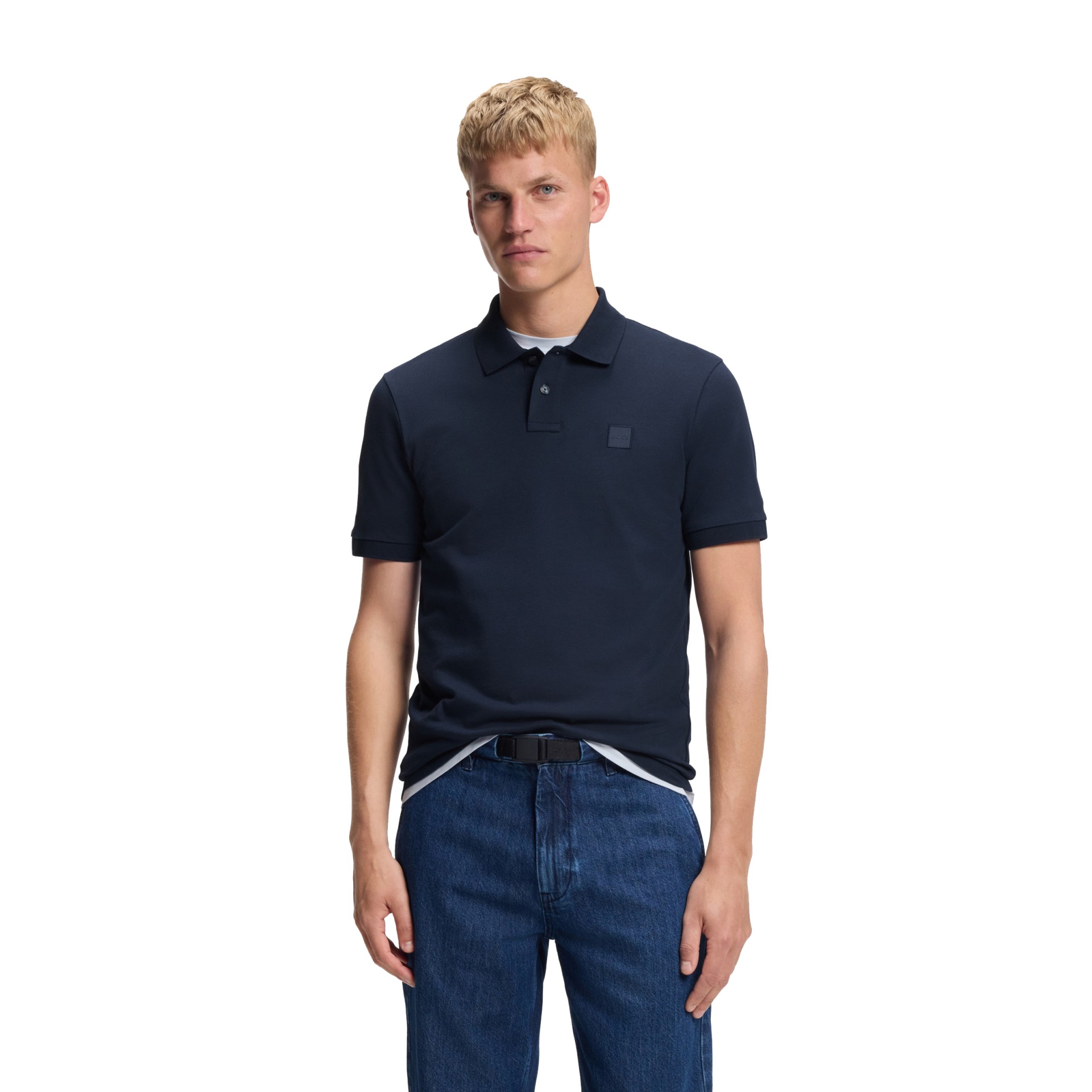 Homem a usar camisa polo azul escuro com logótipo e calças de ganga azul escuro num fundo branco